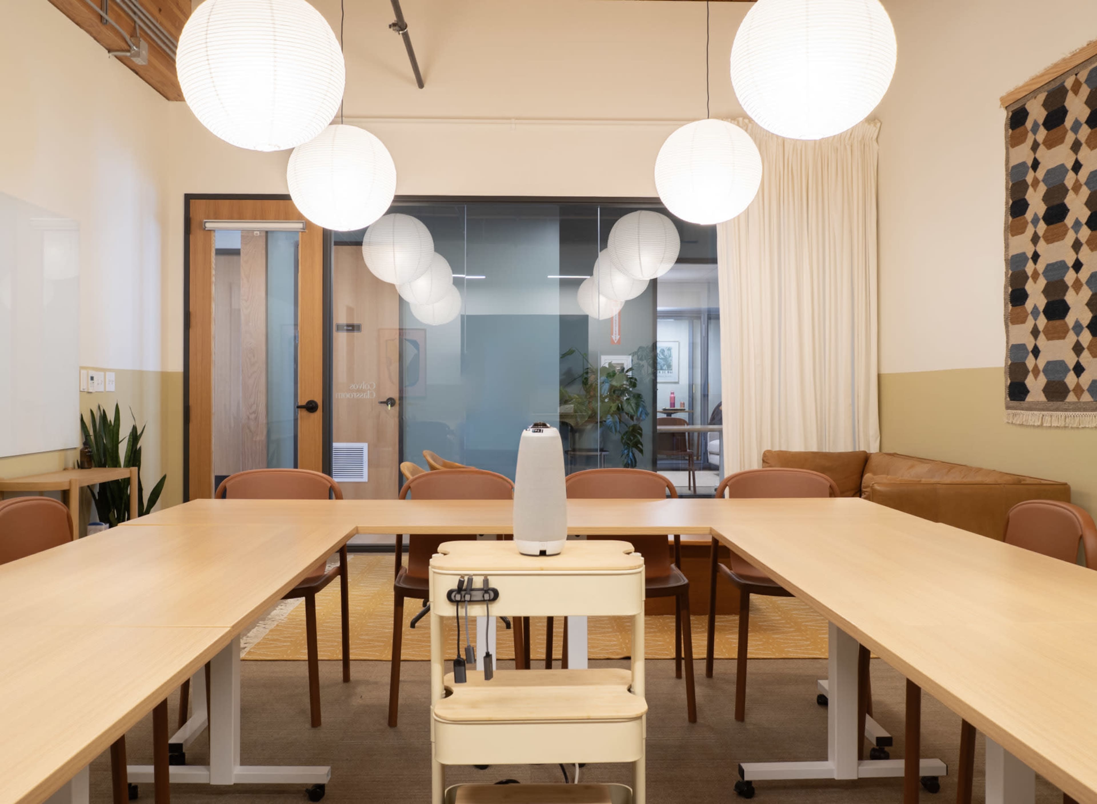 A modern meeting room features a long wooden table, brown chairs, a portable water dispenser, and pendant lights hanging from the ceiling.