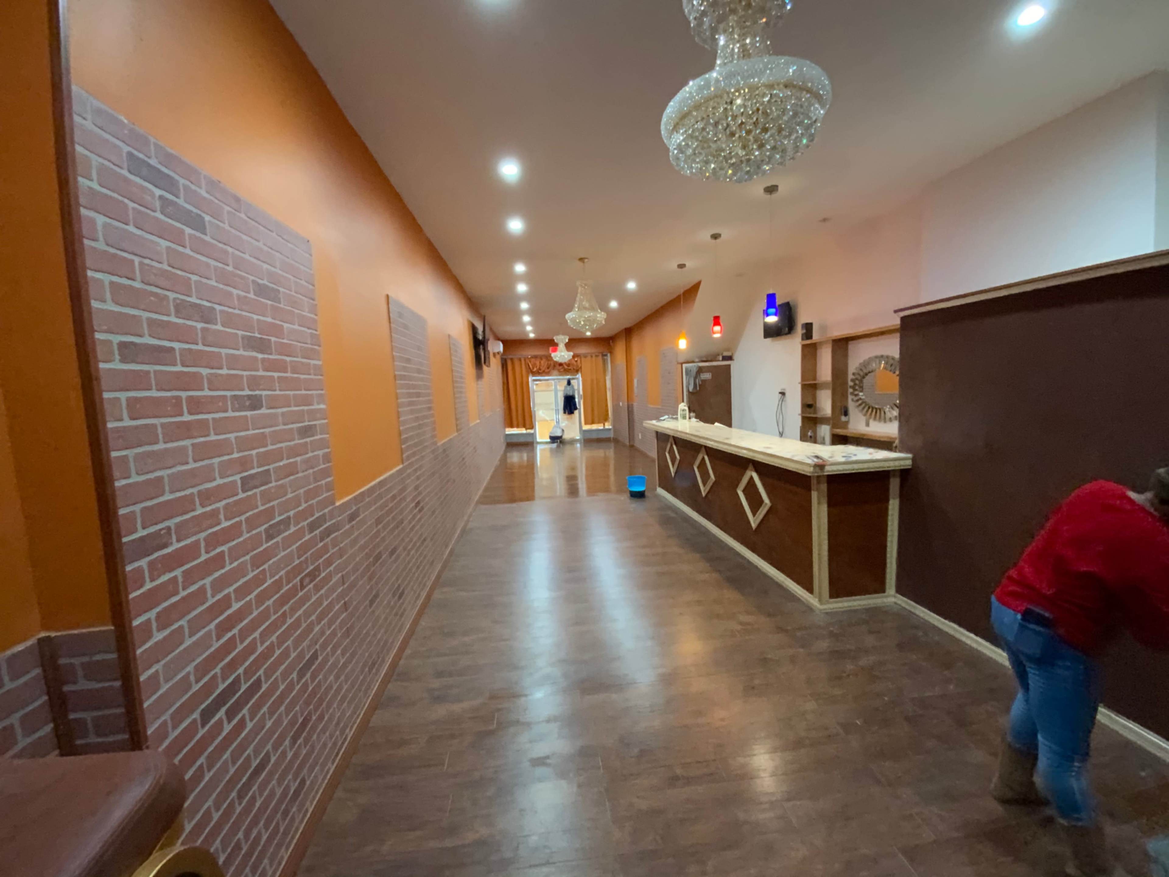 A long, well-lit hallway with wooden flooring, brick-patterned walls on one side, and a counter at the end.