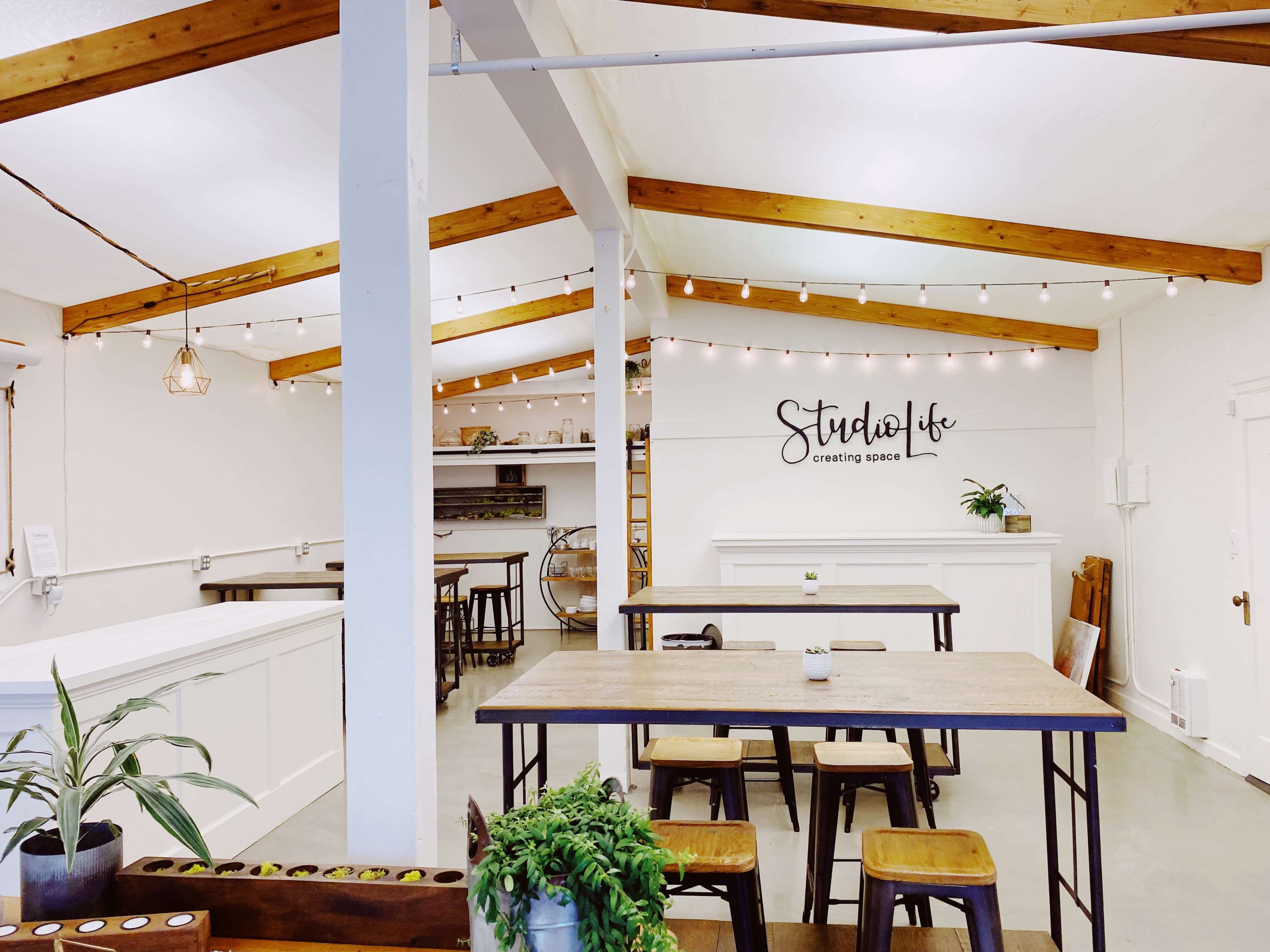 A bright, open interior space with wooden beams, tables, and a wall featuring the phrase "Studio Life - creating space."