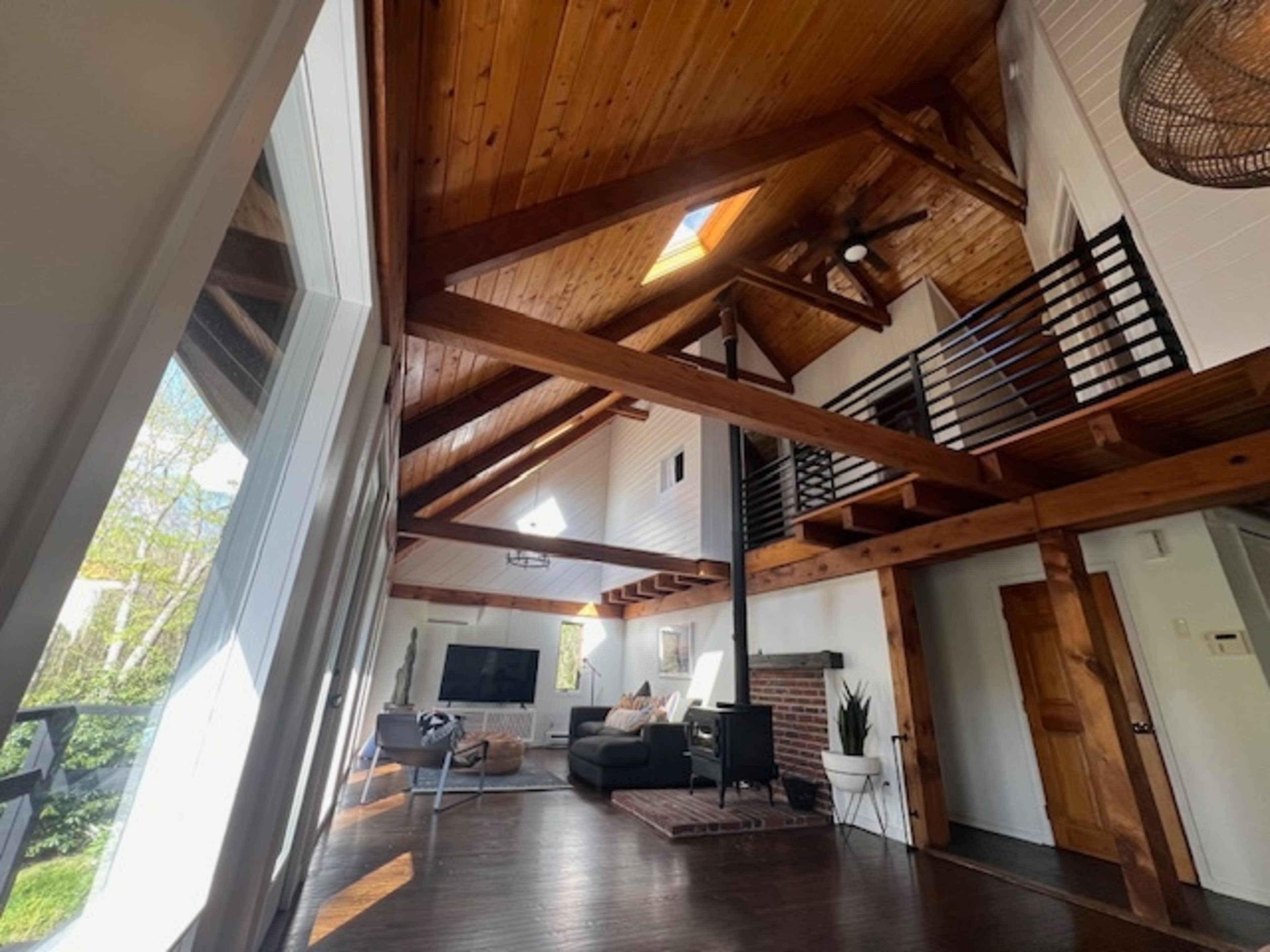 A modern living room with a high wood-beamed ceiling, large windows, and a sectional sofa.