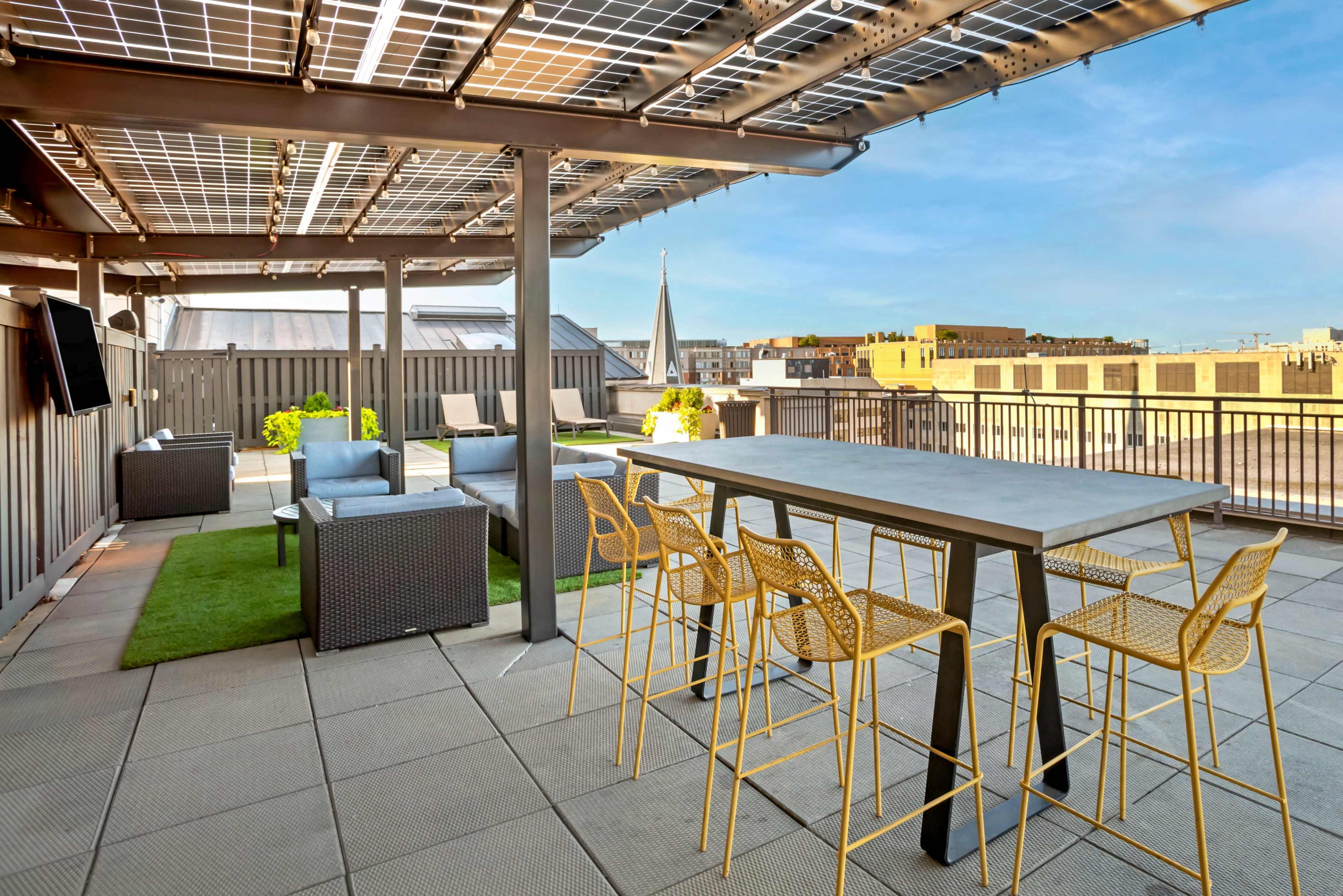 The rooftop terrace features a dining table with yellow chairs, solar panels above, and a view of the surrounding buildings.