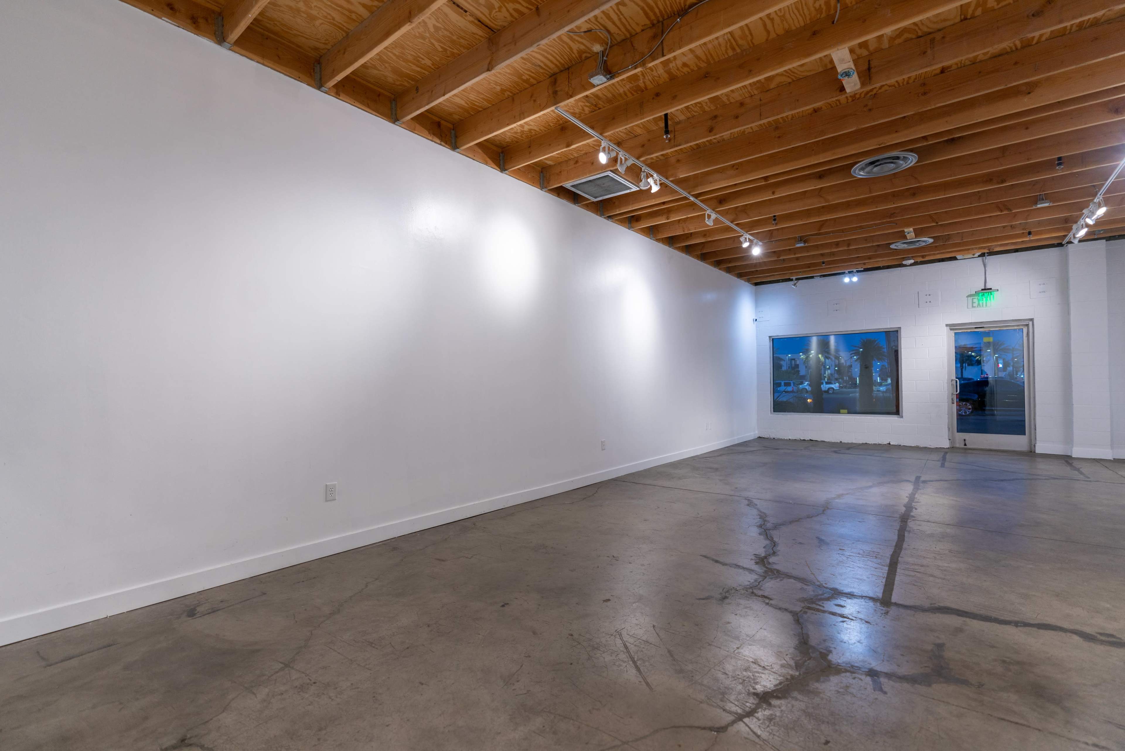 An empty art gallery with white walls, exposed wooden beams, and a polished concrete floor.