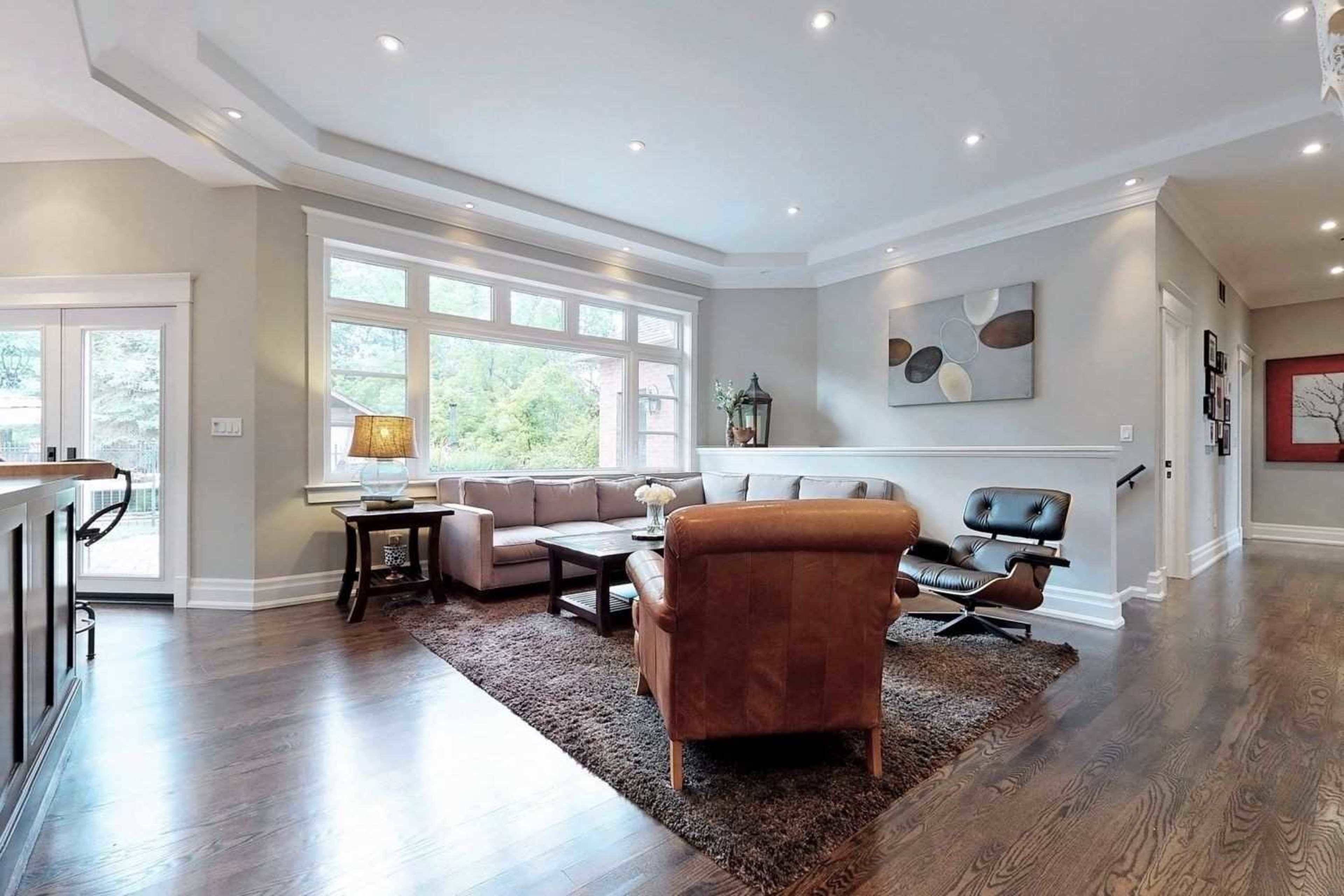 A spacious living room features a sectional sofa, two chairs, and large windows that allow natural light to illuminate the hardwood floors.