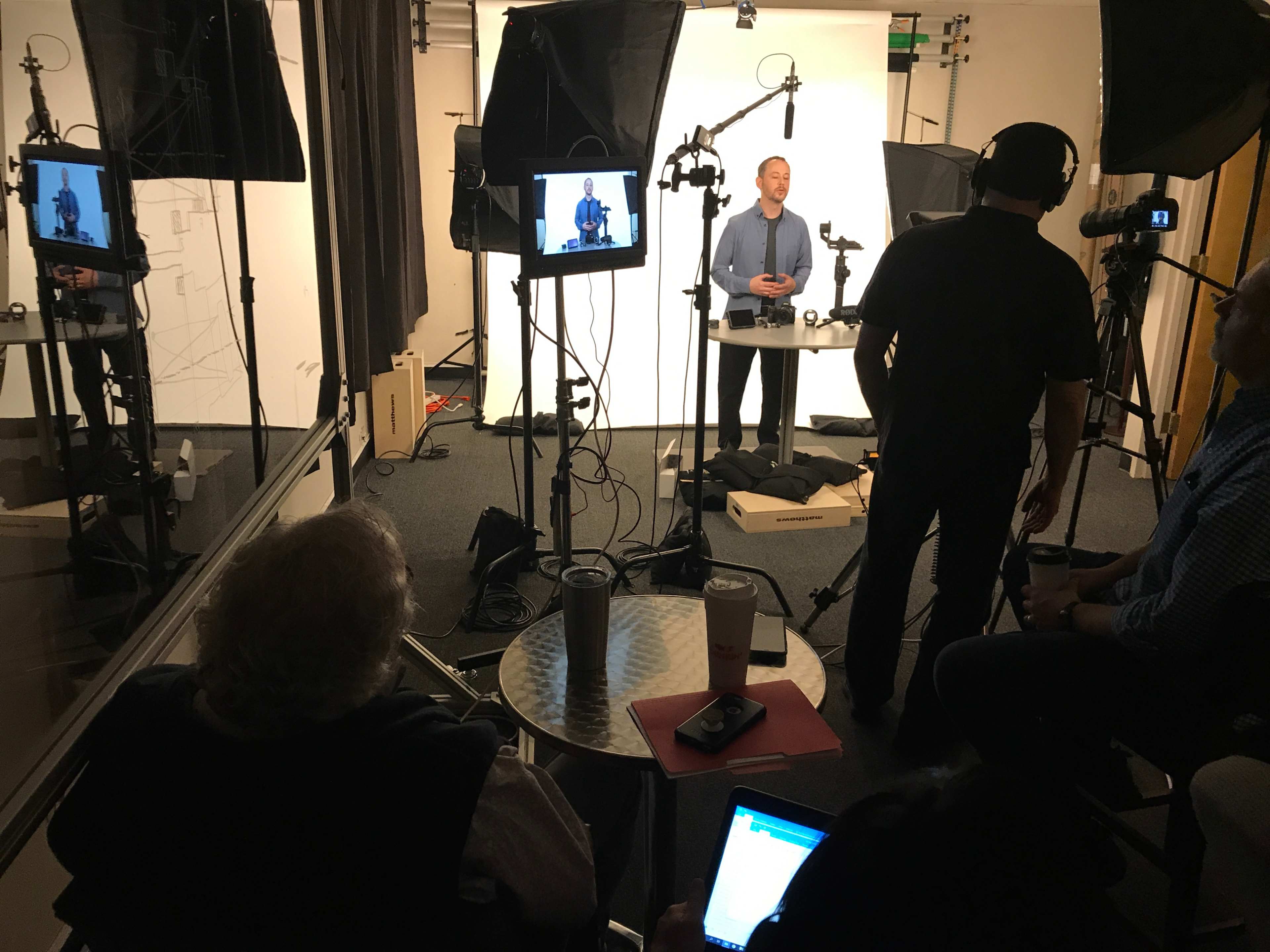 A man is speaking in front of a camera while being recorded in a studio setup with multiple lighting and equipment.