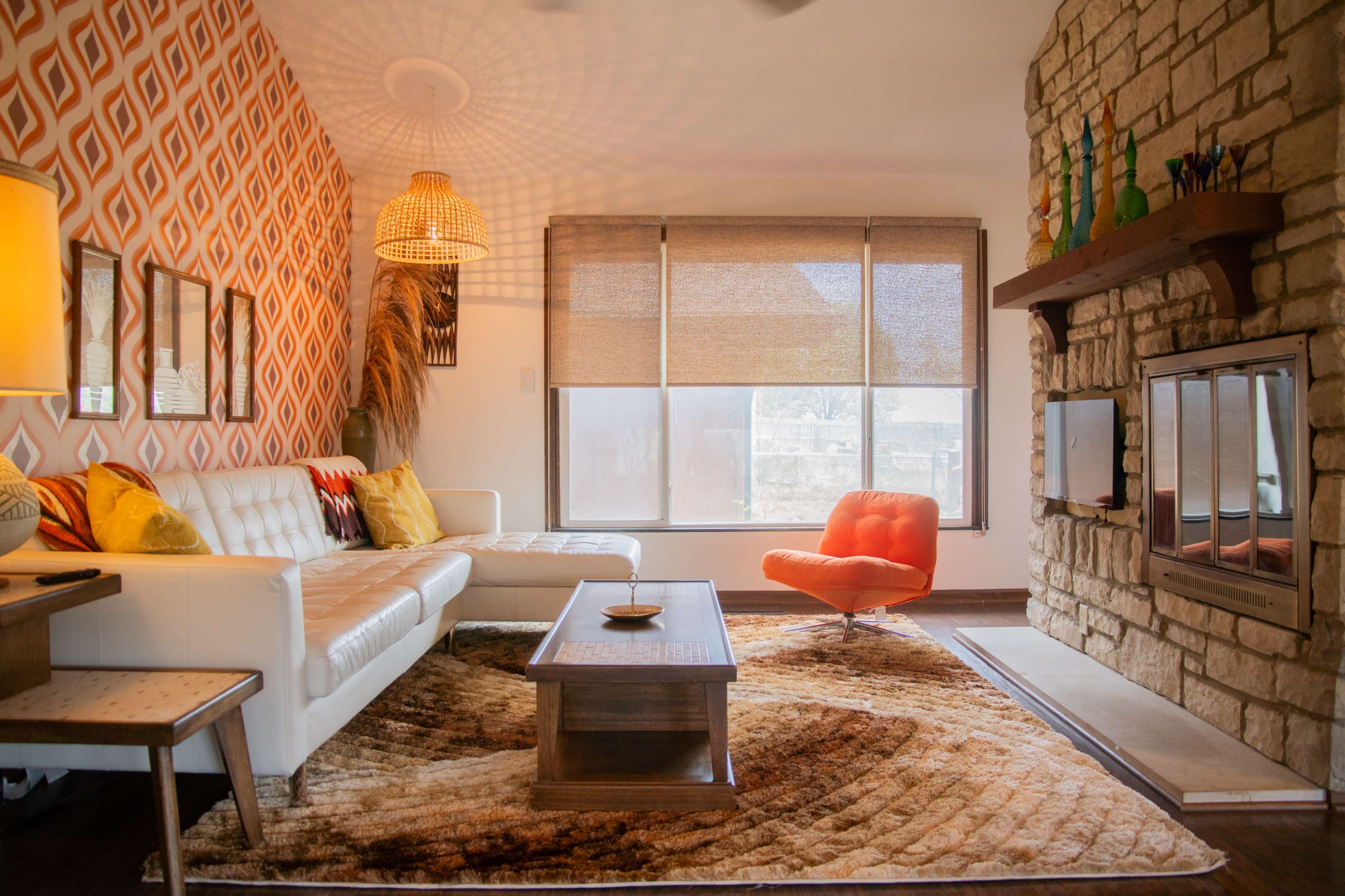 The image depicts a modern living room with a white sofa, an orange accent chair, a stone fireplace, and patterned wallpaper.