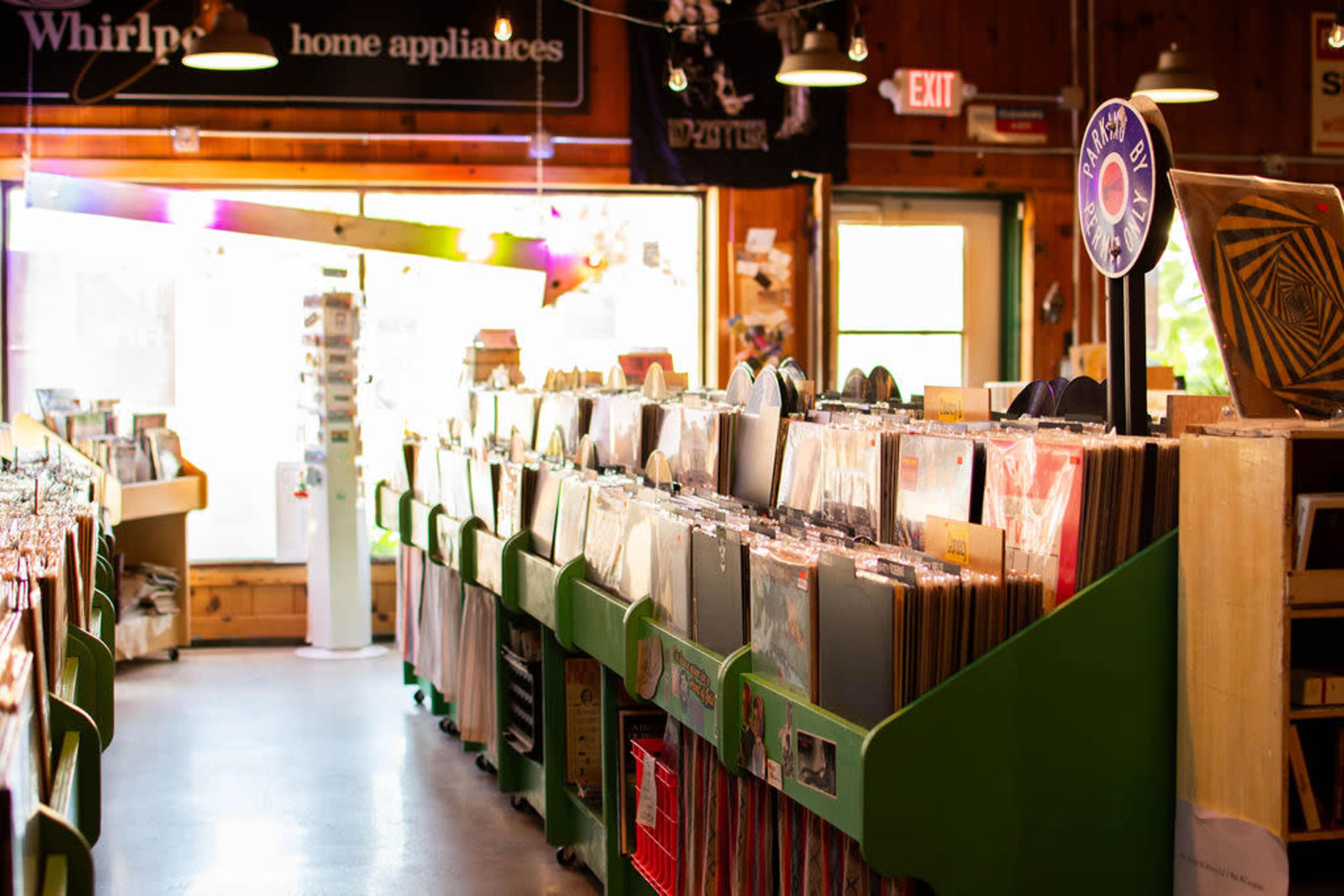 The image shows the interior of a record store with rows of display bins filled with vinyl records.