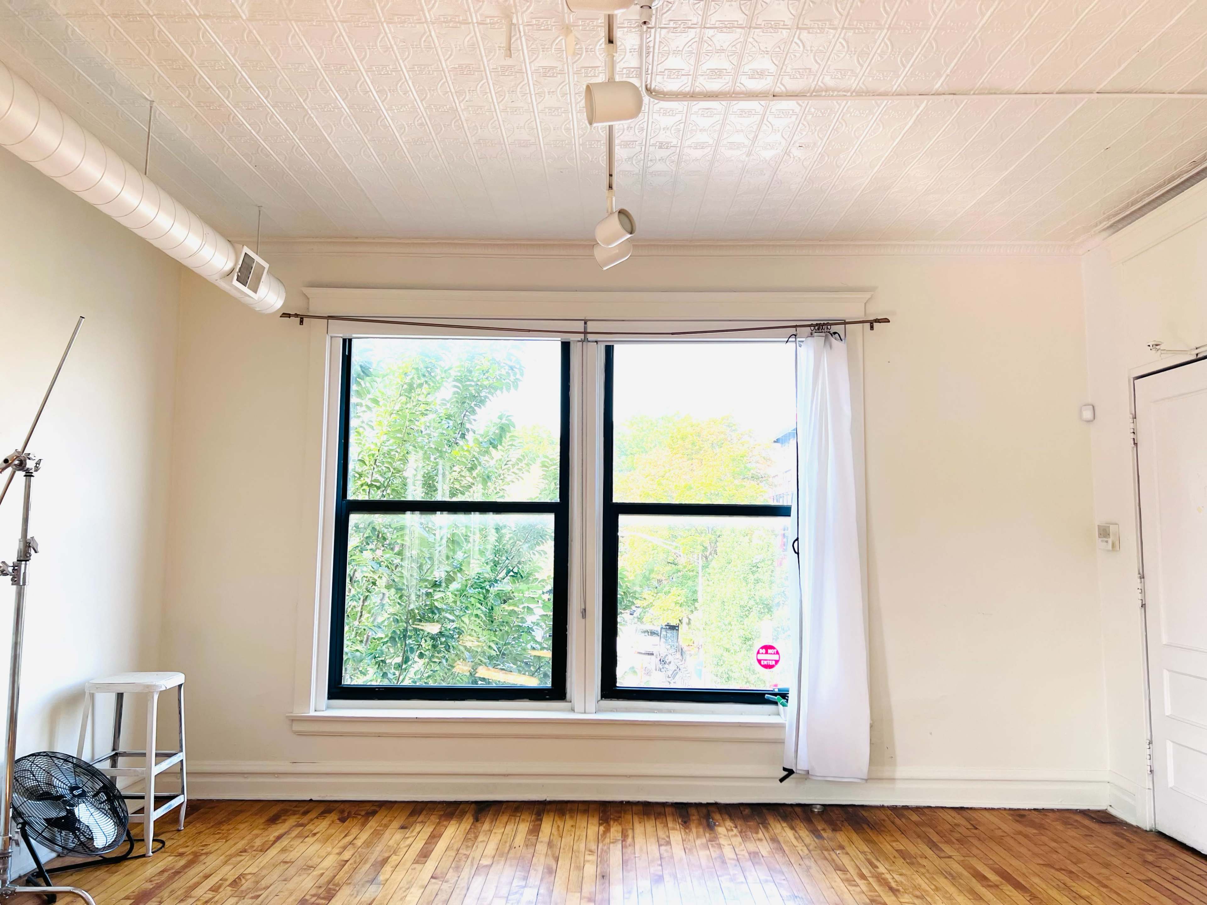 A spacious room with wooden floors features a large window dressed with a sheer curtain, allowing natural light to fill the space.