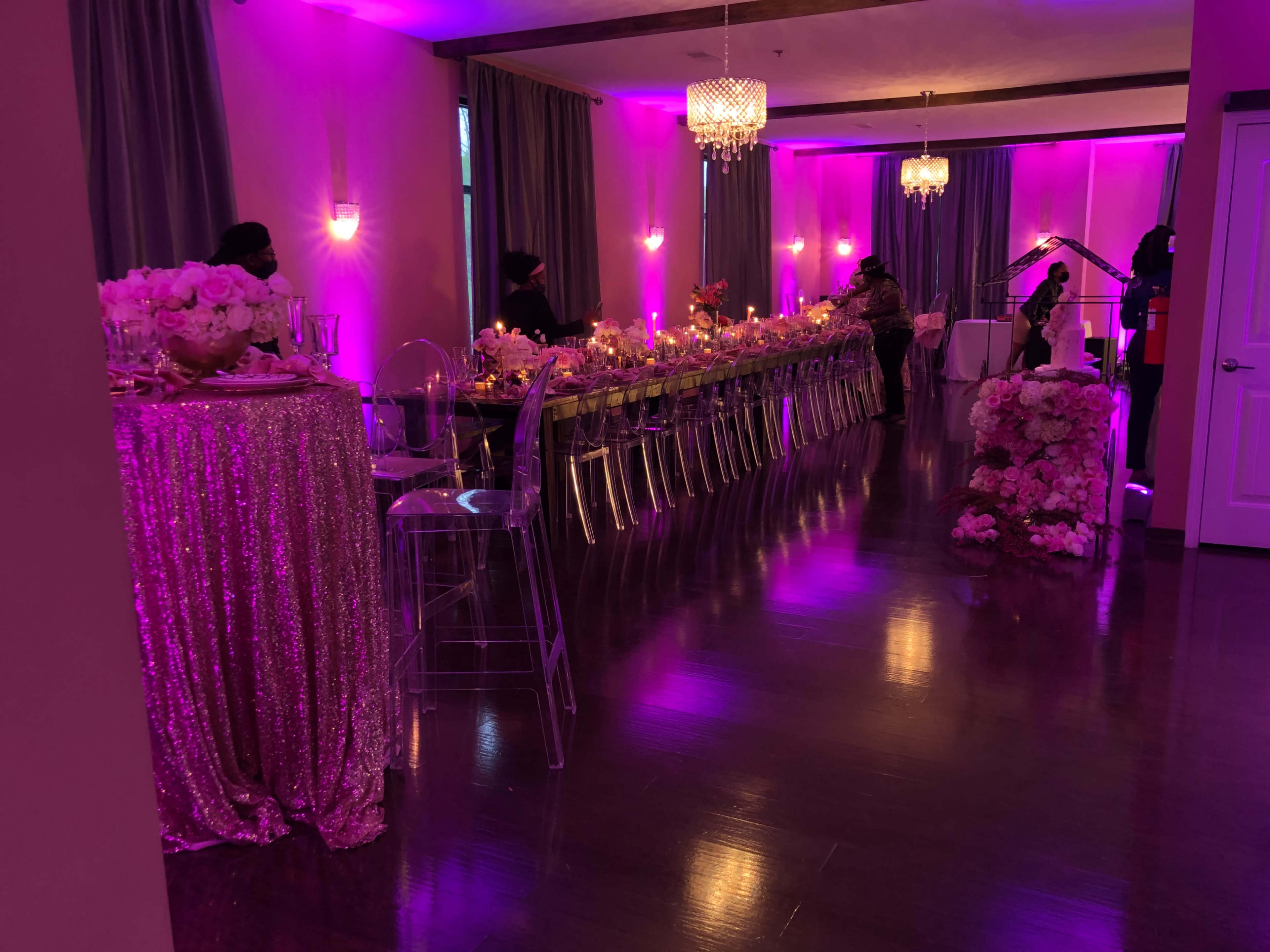The scene shows a banquet hall with a long table set for a formal event, illuminated by purple lights and decorated with floral arrangements.