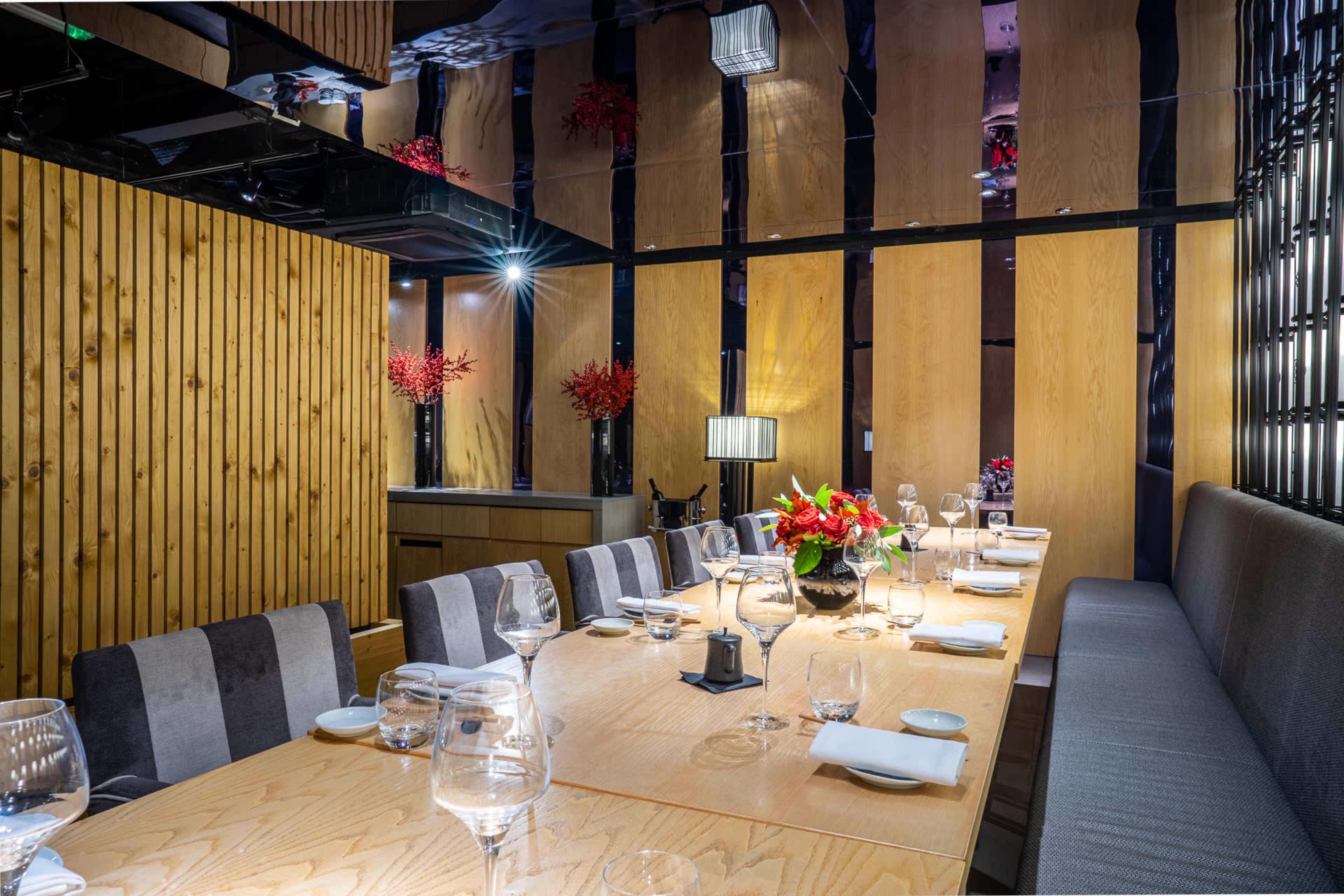 A private dining room features a long wooden table set with glassware and elegant decorations, surrounded by wooden walls and low lighting.
