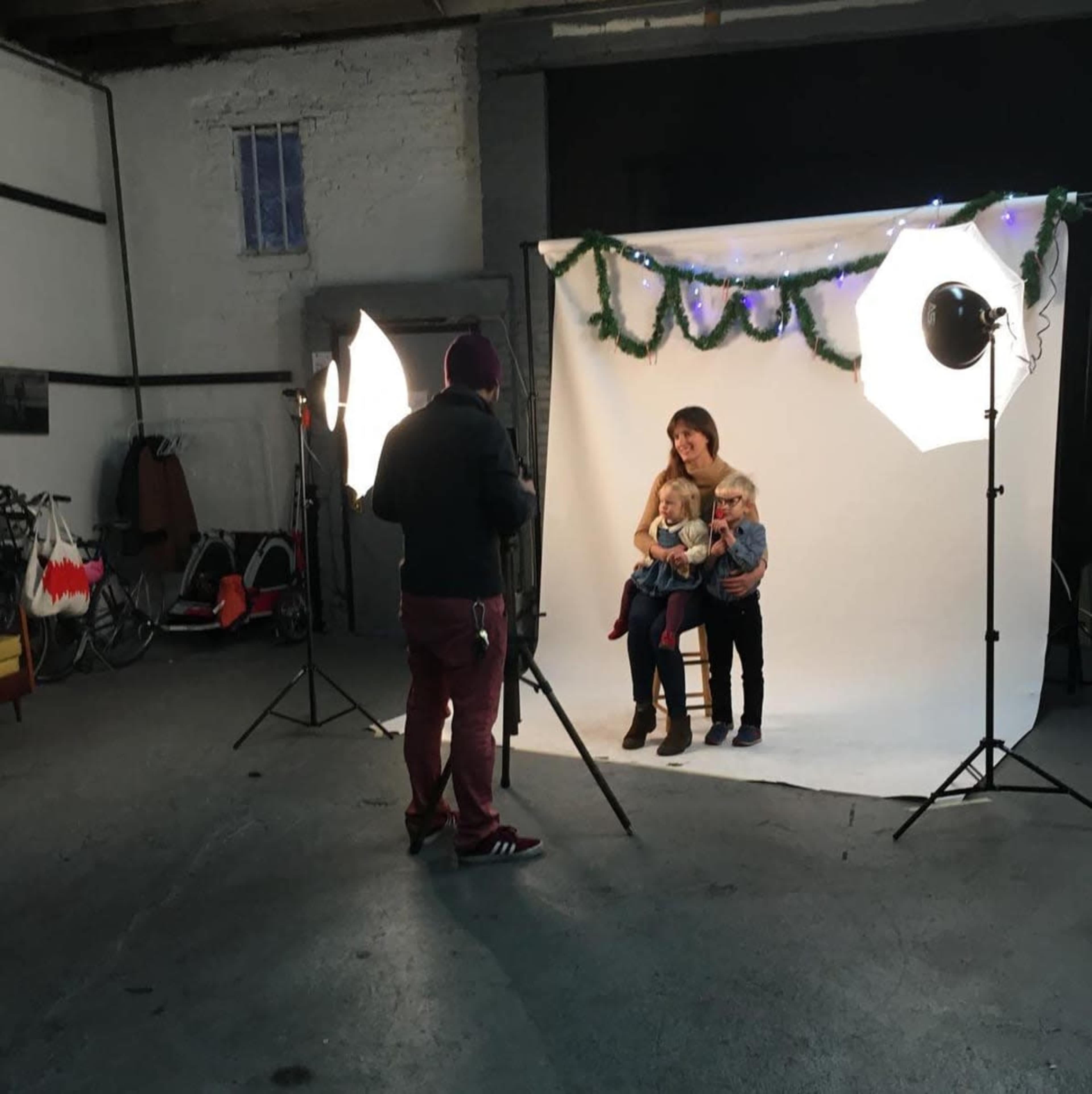 A photographer is capturing a family portrait in a studio setting with a white backdrop and professional lighting equipment.
