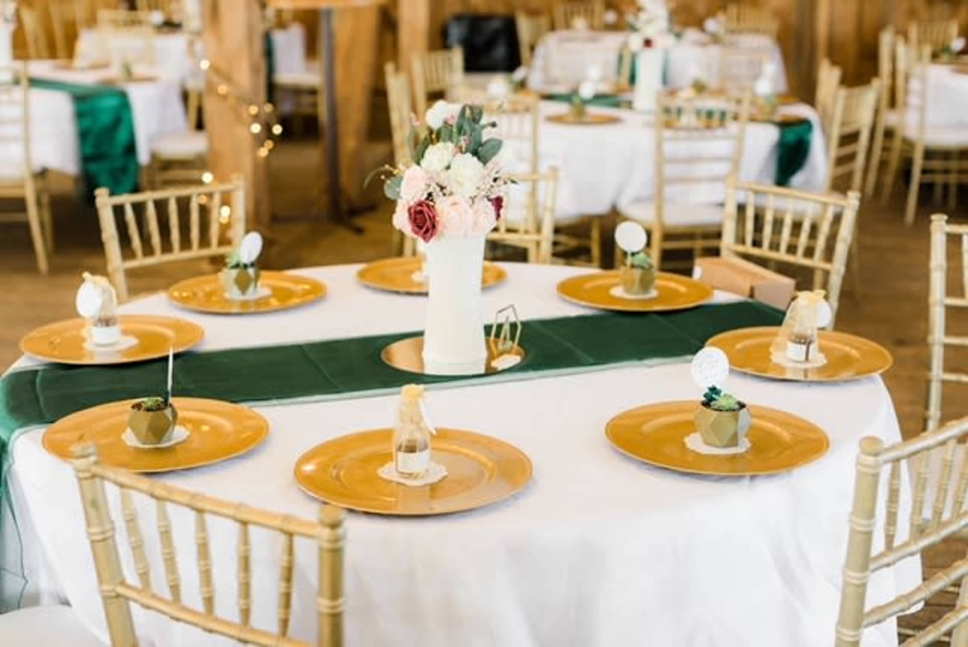 A round dining table is set with gold plates and decorative centerpieces in a venue adorned with wooden accents.
