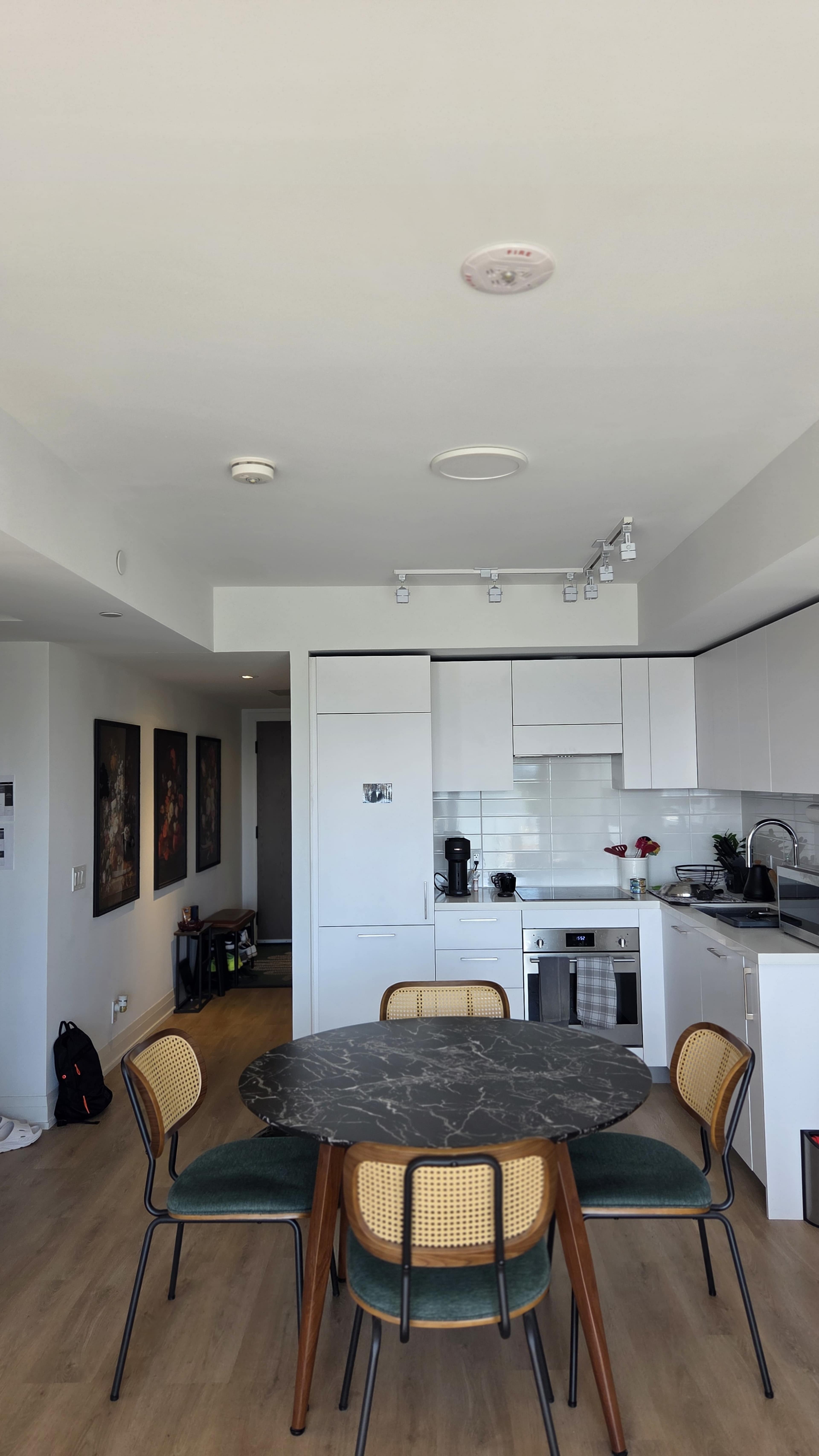 A modern kitchen and dining area features a round marble table surrounded by four chairs, with white cabinetry and a stainless steel kitchen setup in the background.