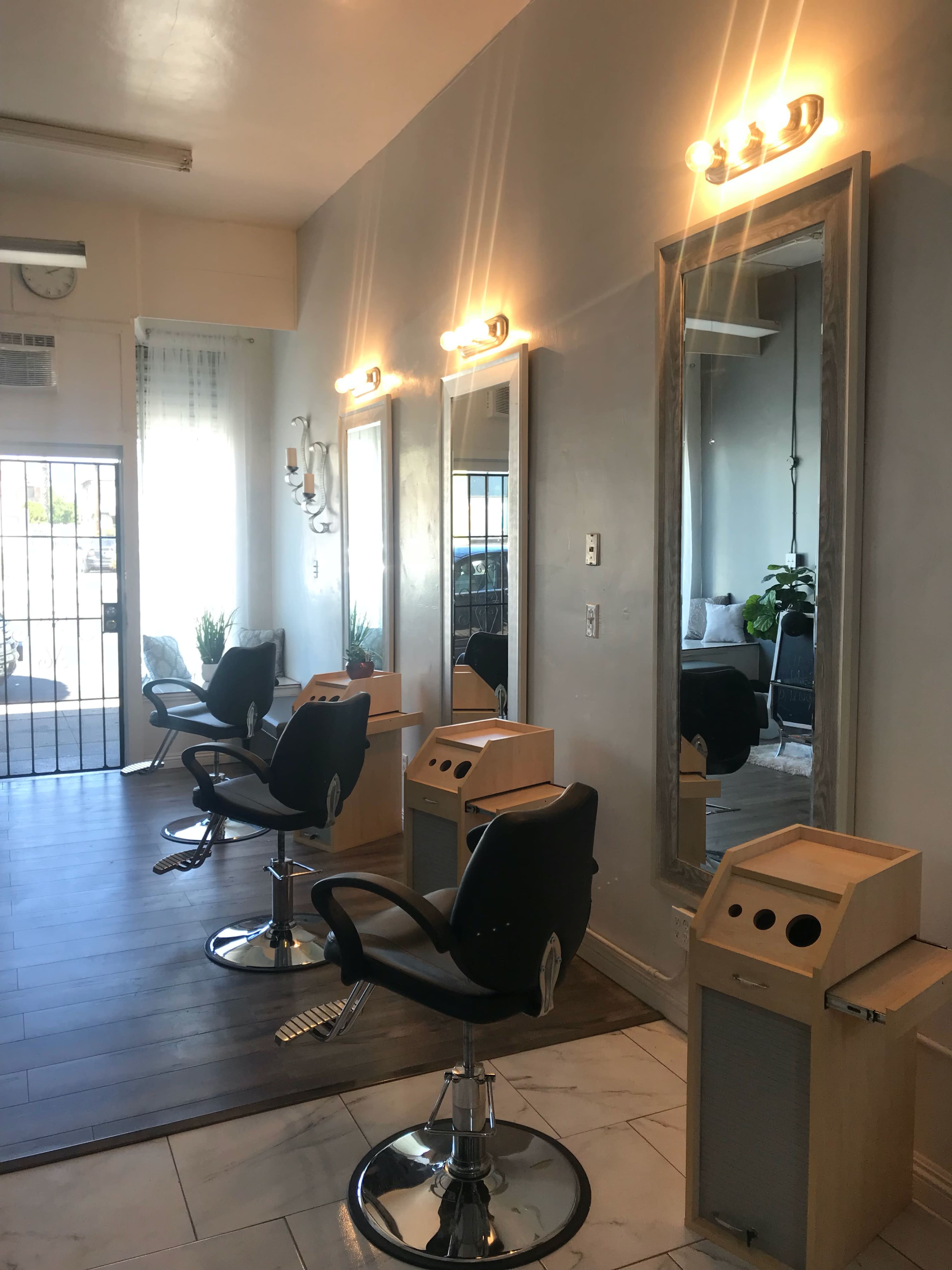A modern hair salon with three styling stations, each featuring a mirror and a chair, along with lighted fixtures and wooden accents.