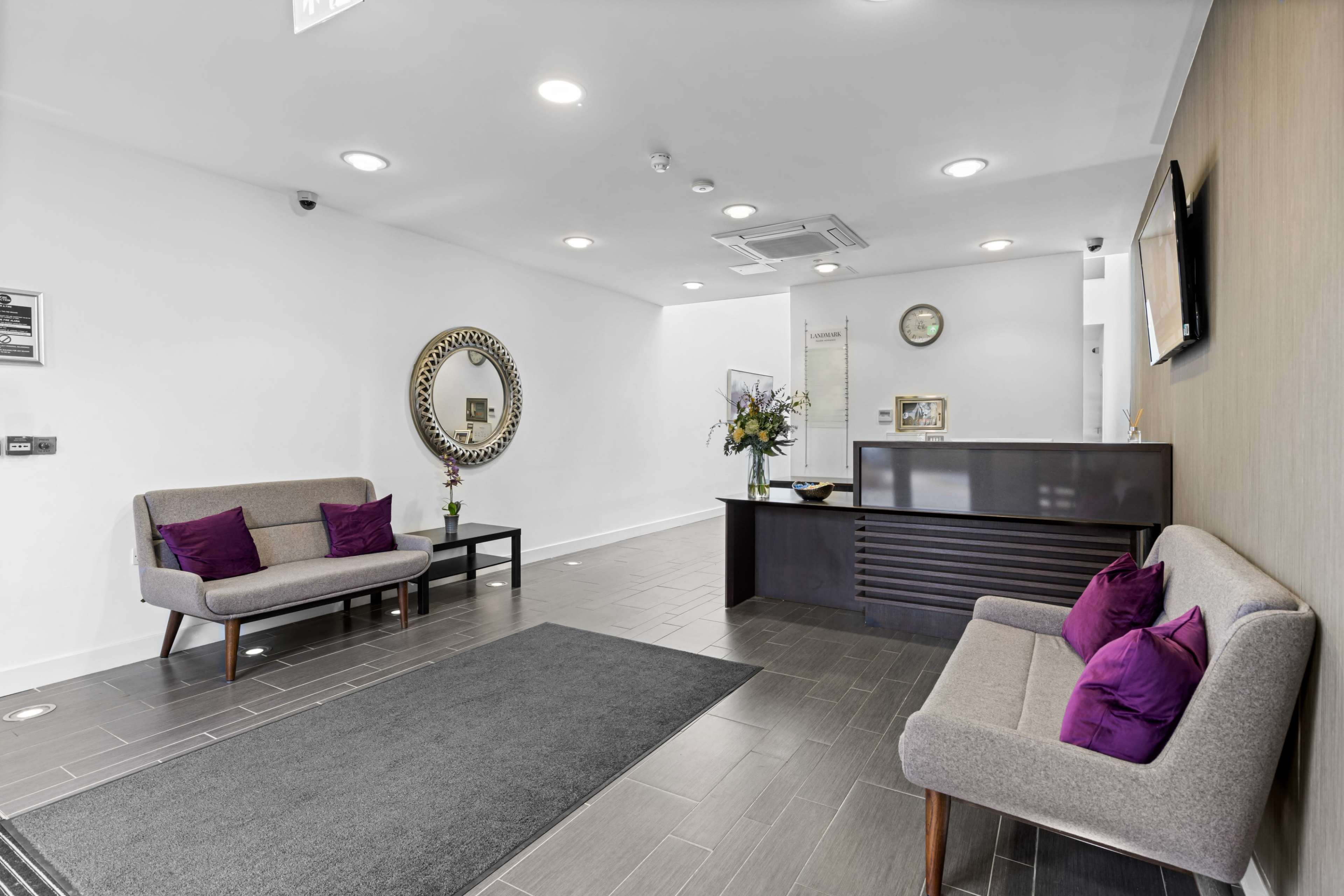 A modern lobby area with two upholstered sofas, a reception desk, and decorative elements including a mirror and flowers.