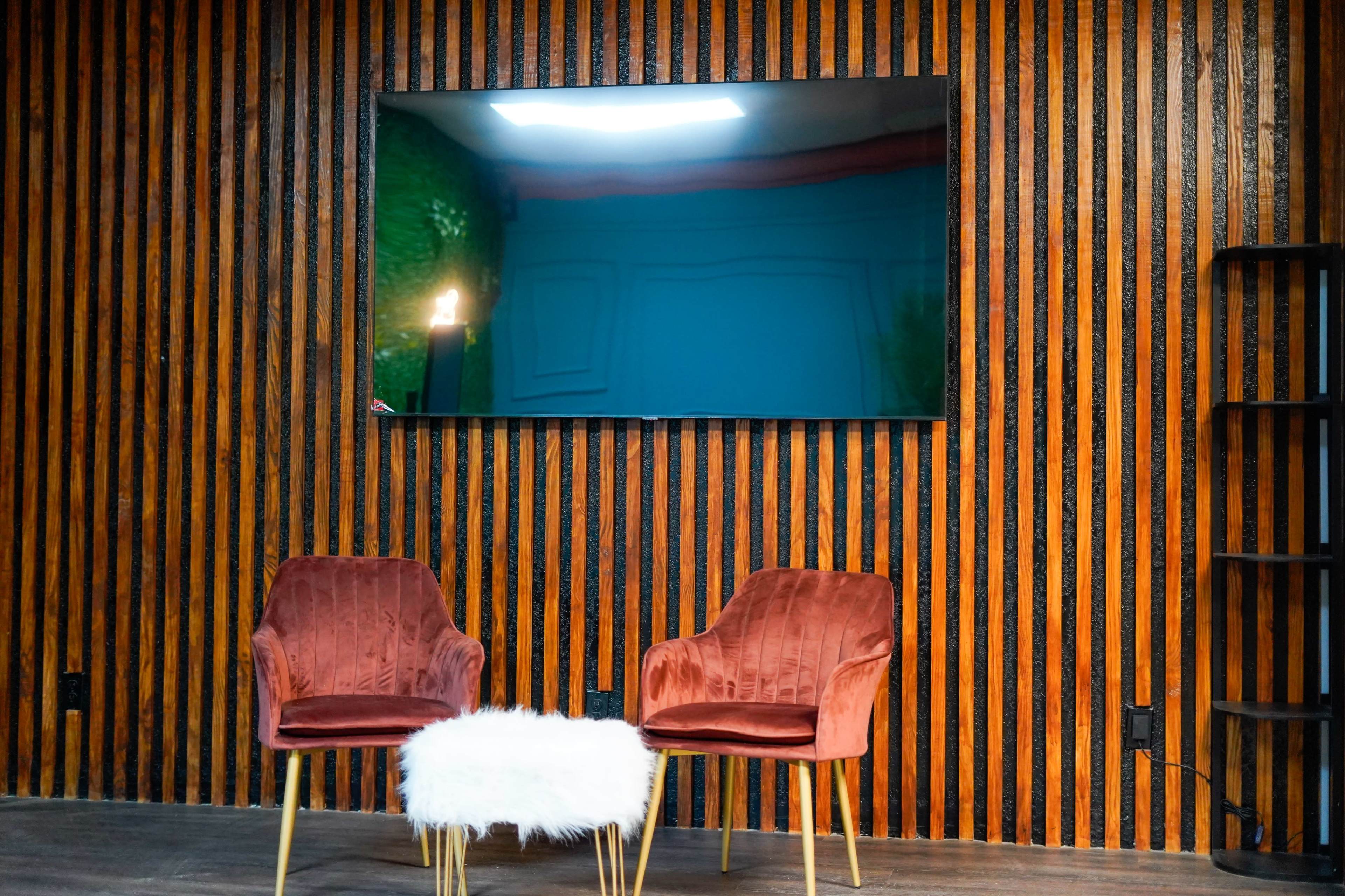 Two velvety chairs with a small fur-covered table in front of a large flat-screen TV mounted on a wooden striped wall.