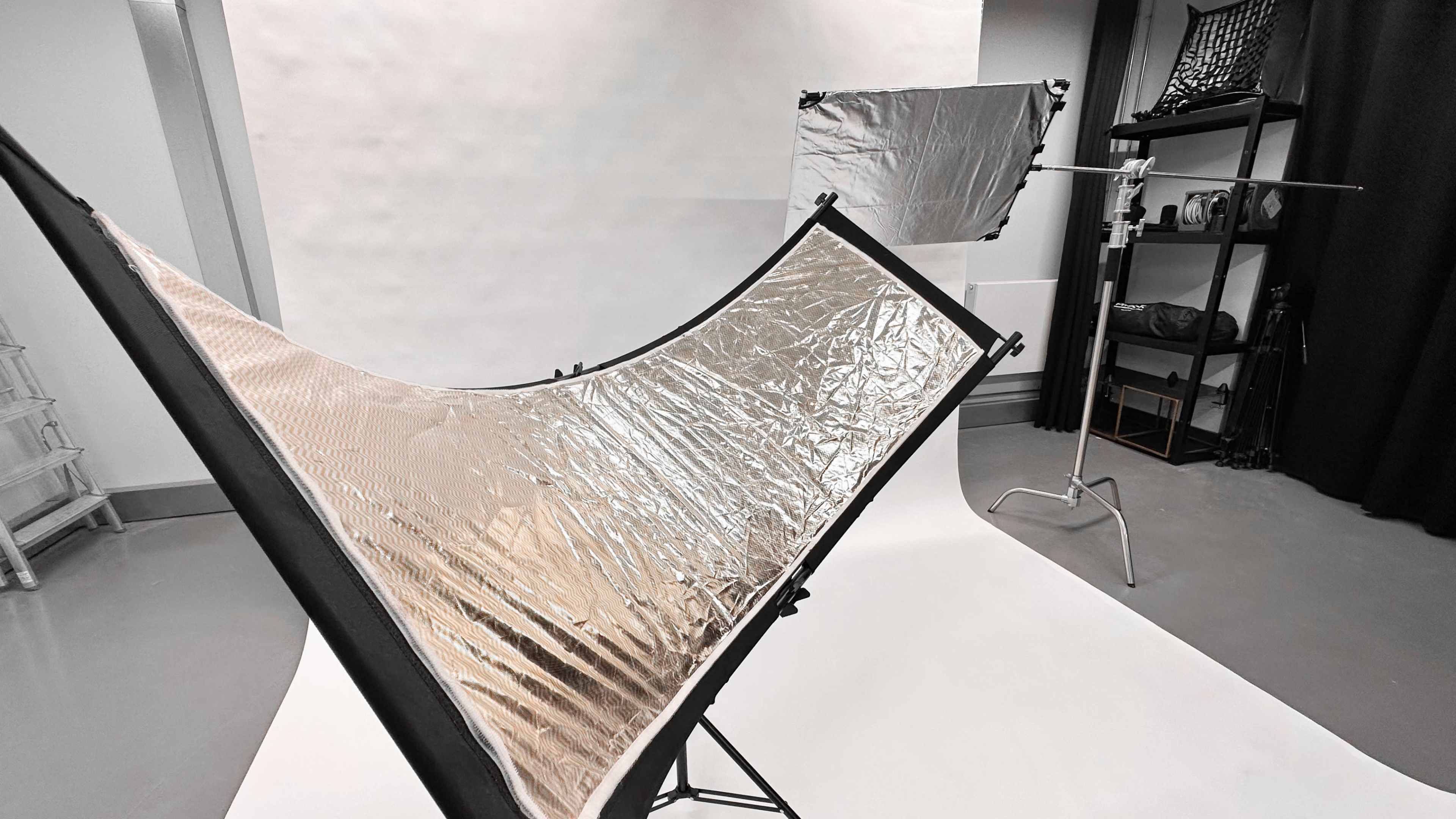 A photography setup featuring a large reflector with a shiny surface and a backdrop in a studio environment.
