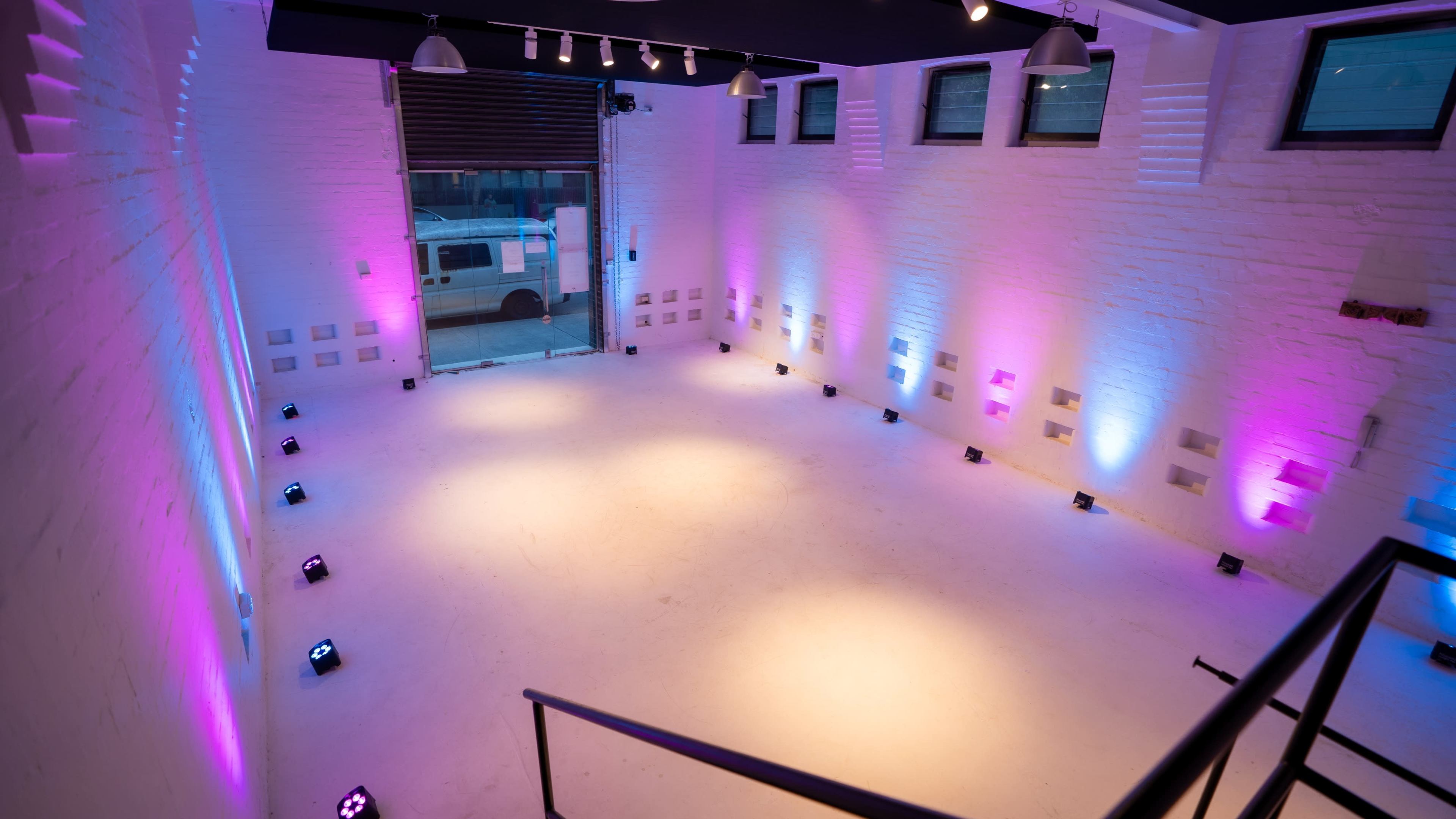 A bright, empty event space with white walls and colored lighting along the perimeter.