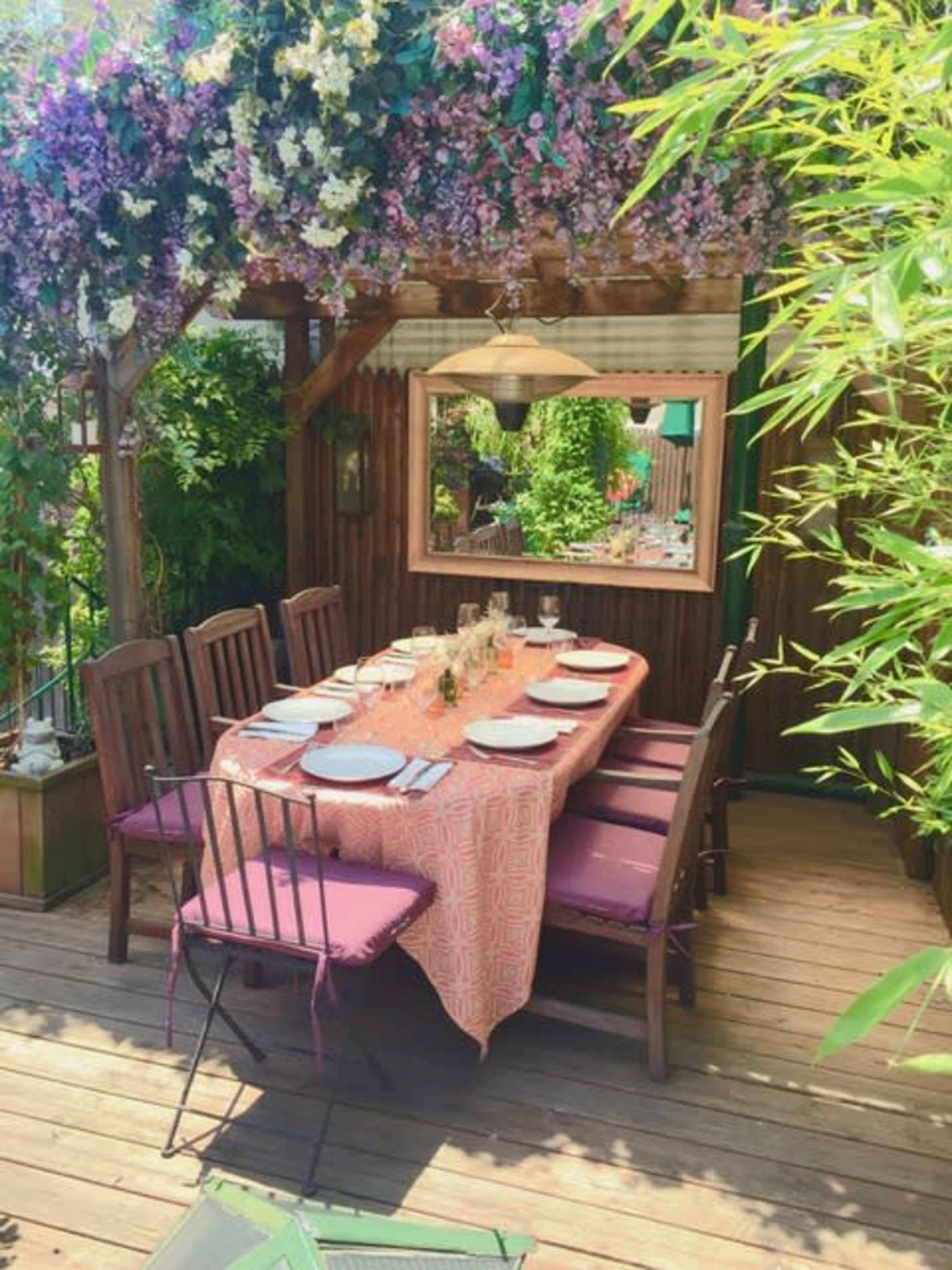 A wooden patio features a table set with plates and glassware beneath a floral canopy.