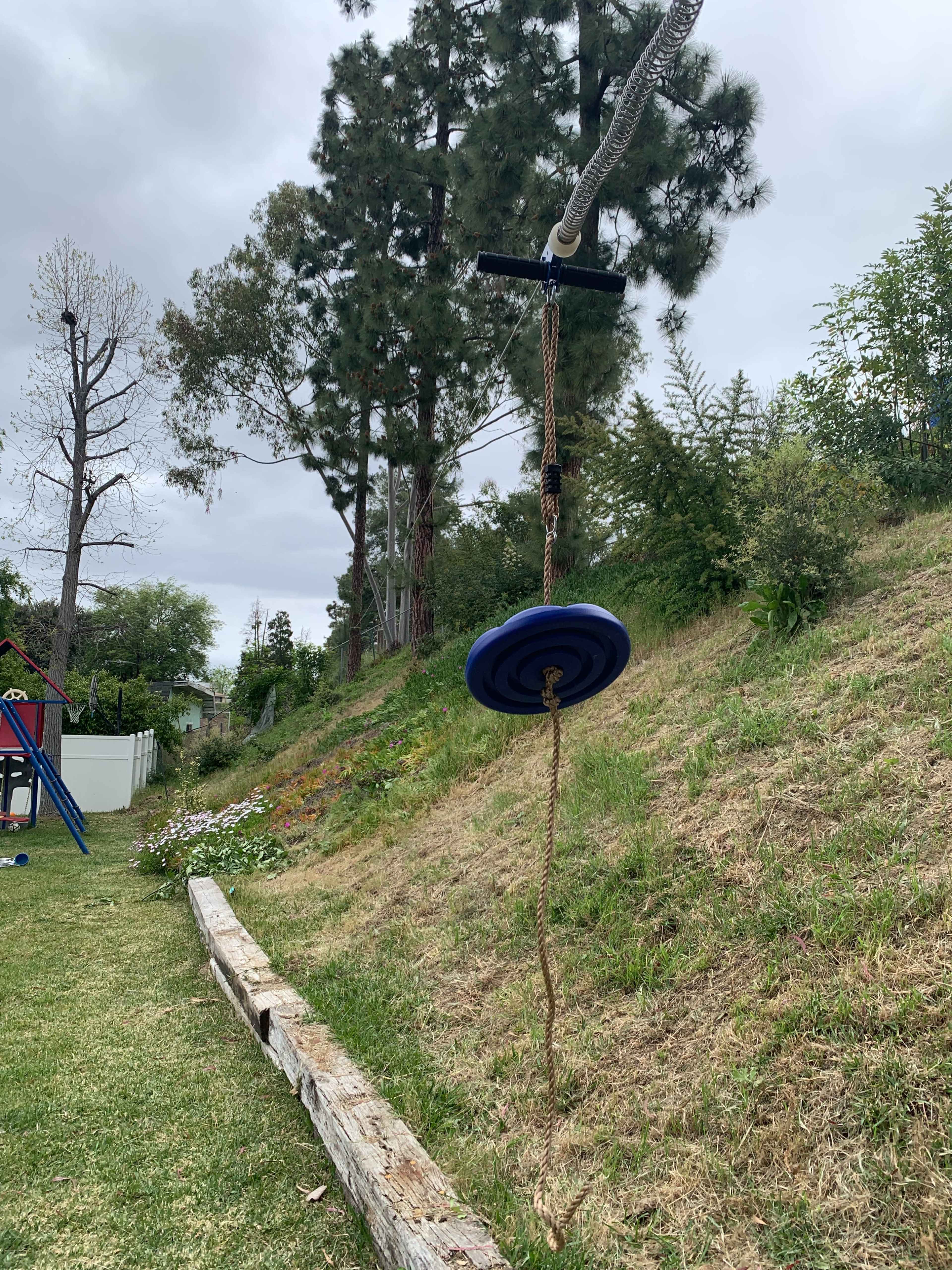 A blue disc is attached to a rope hanging from a pulley on a sloped grassy area beside a wooden beam.