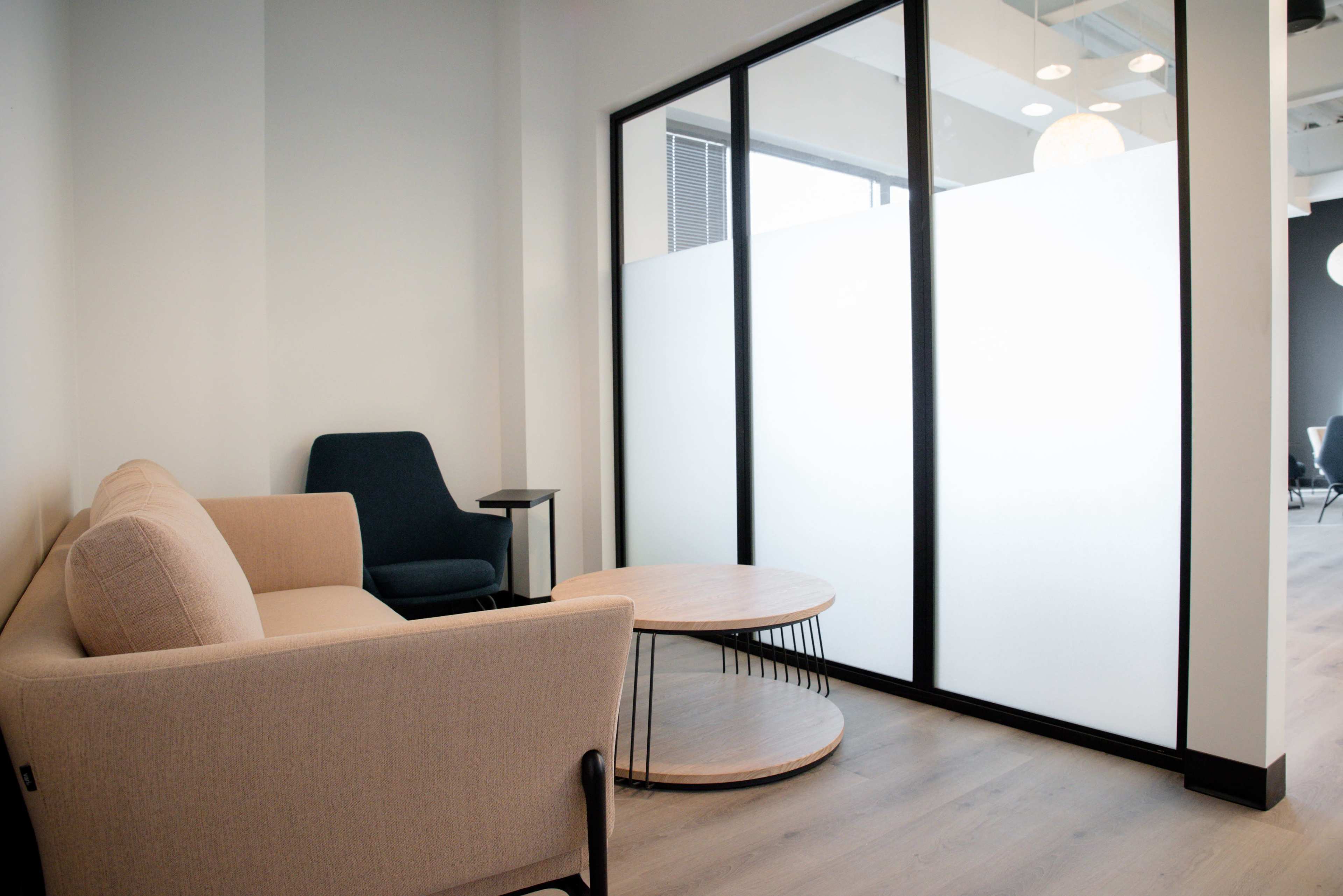 The image shows a modern interior space featuring a light-colored couch, a dark chair, and a round coffee table in front of a frosted glass partition.