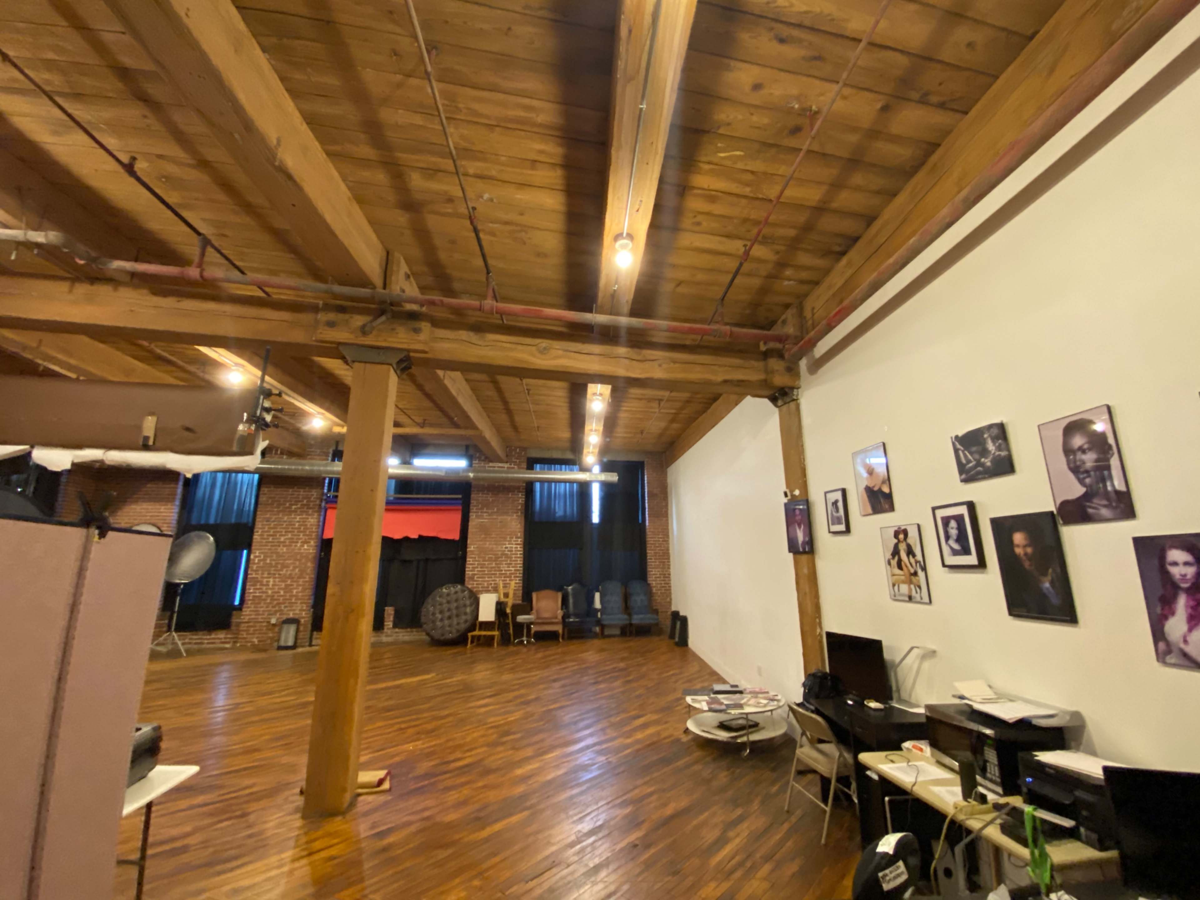A spacious studio with wooden beams and a polished floor, featuring various seating arrangements and photographs on the walls.