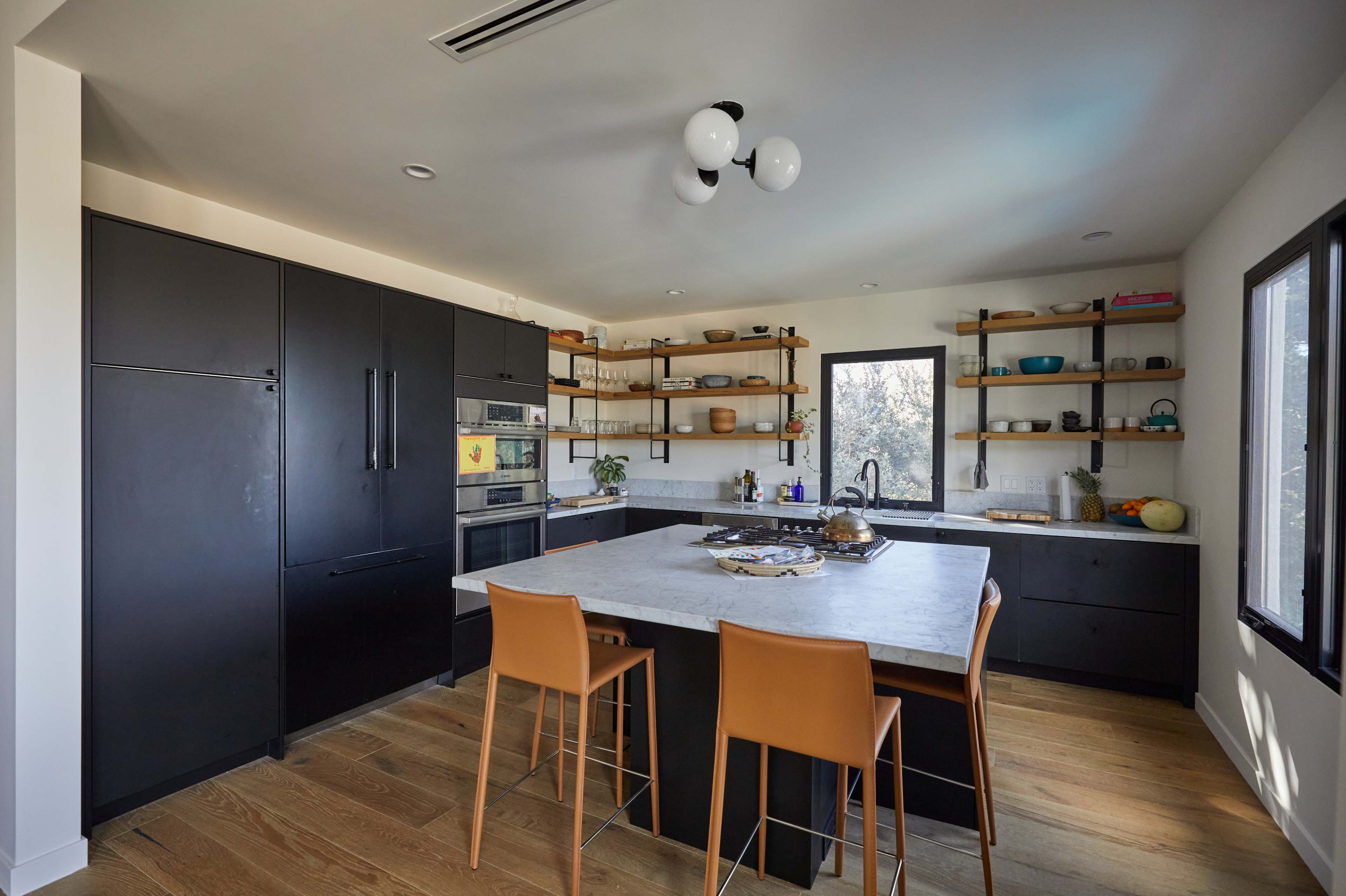 The kitchen features black cabinetry, a large marble island with bar seating, and open shelving displaying cookware and decorative items.