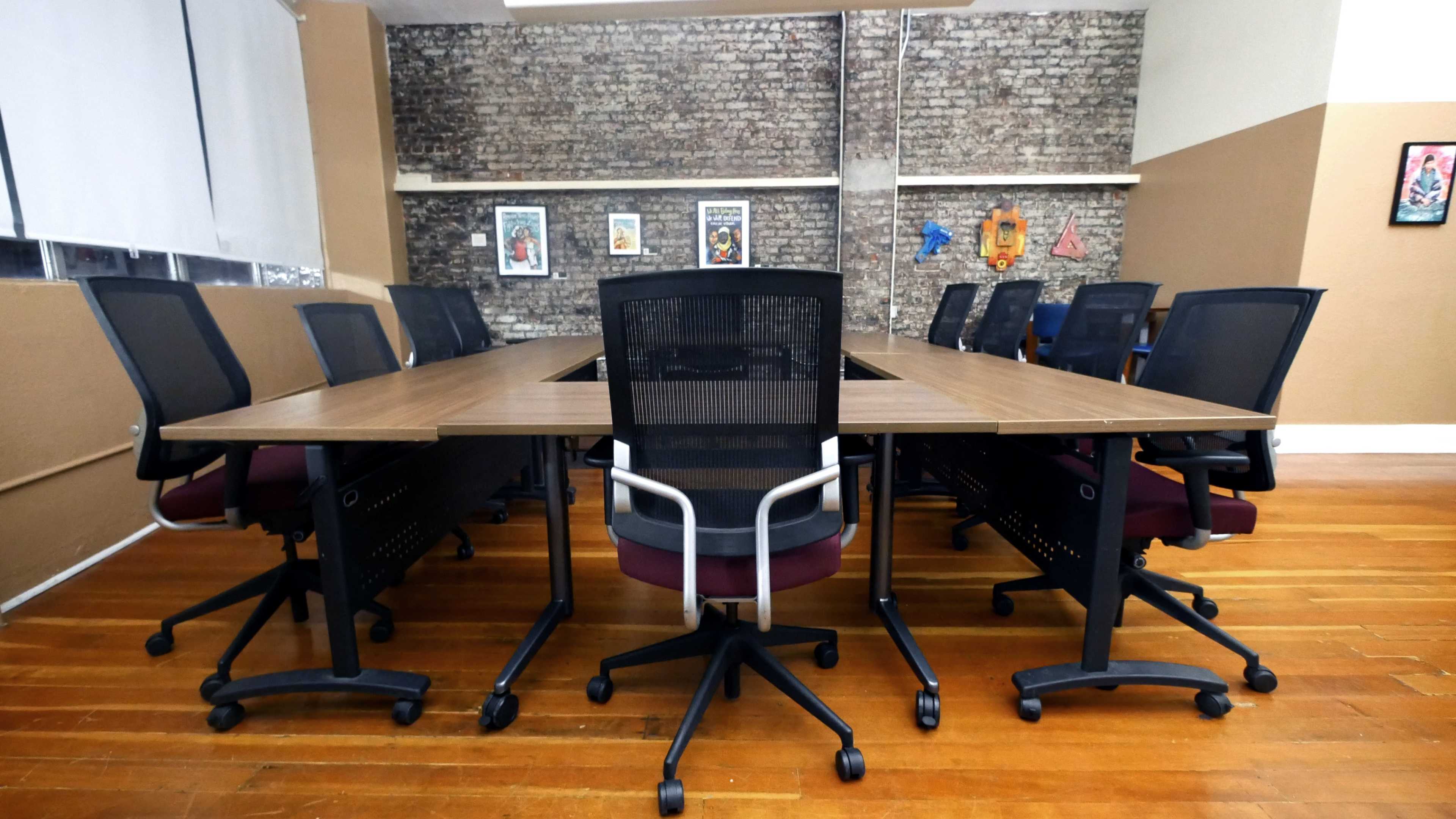 A large conference table surrounded by black office chairs is set in a room with exposed brick walls and artwork.