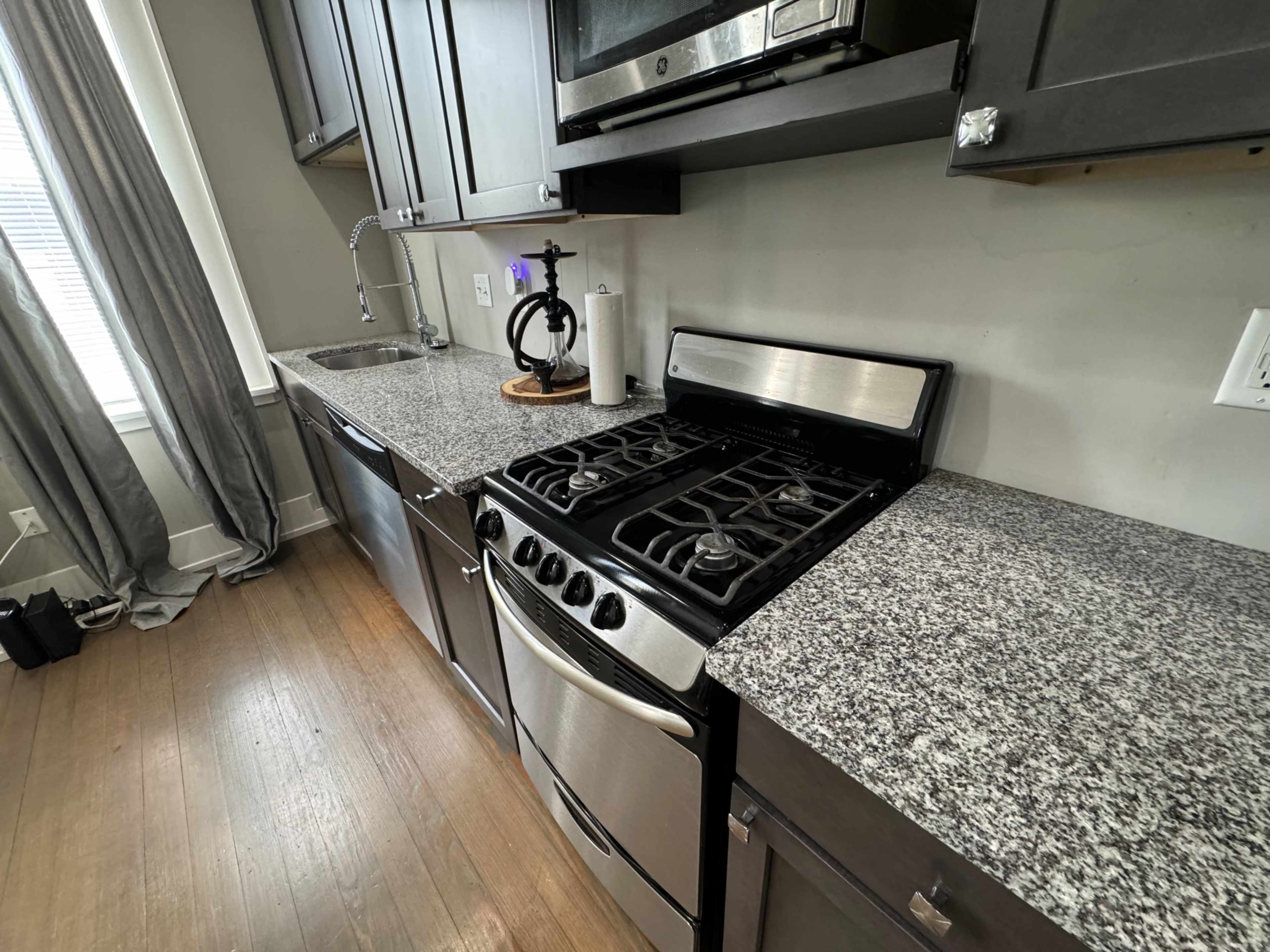 A kitchen with dark cabinets, a stainless steel stove, a microwave above, and a granite countertop.