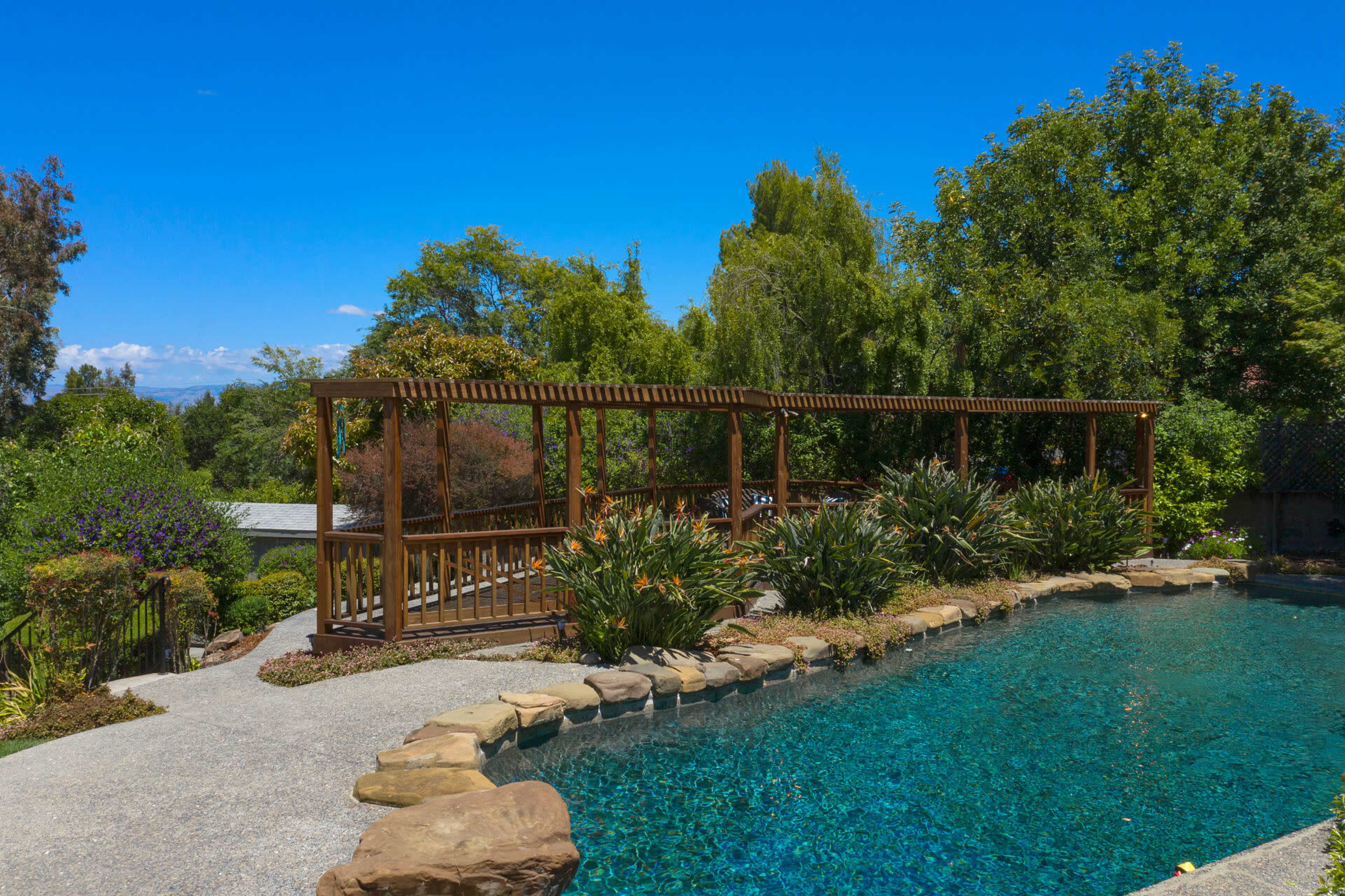 A landscaped garden with a clear pool surrounded by rocks and a wooden pergola.