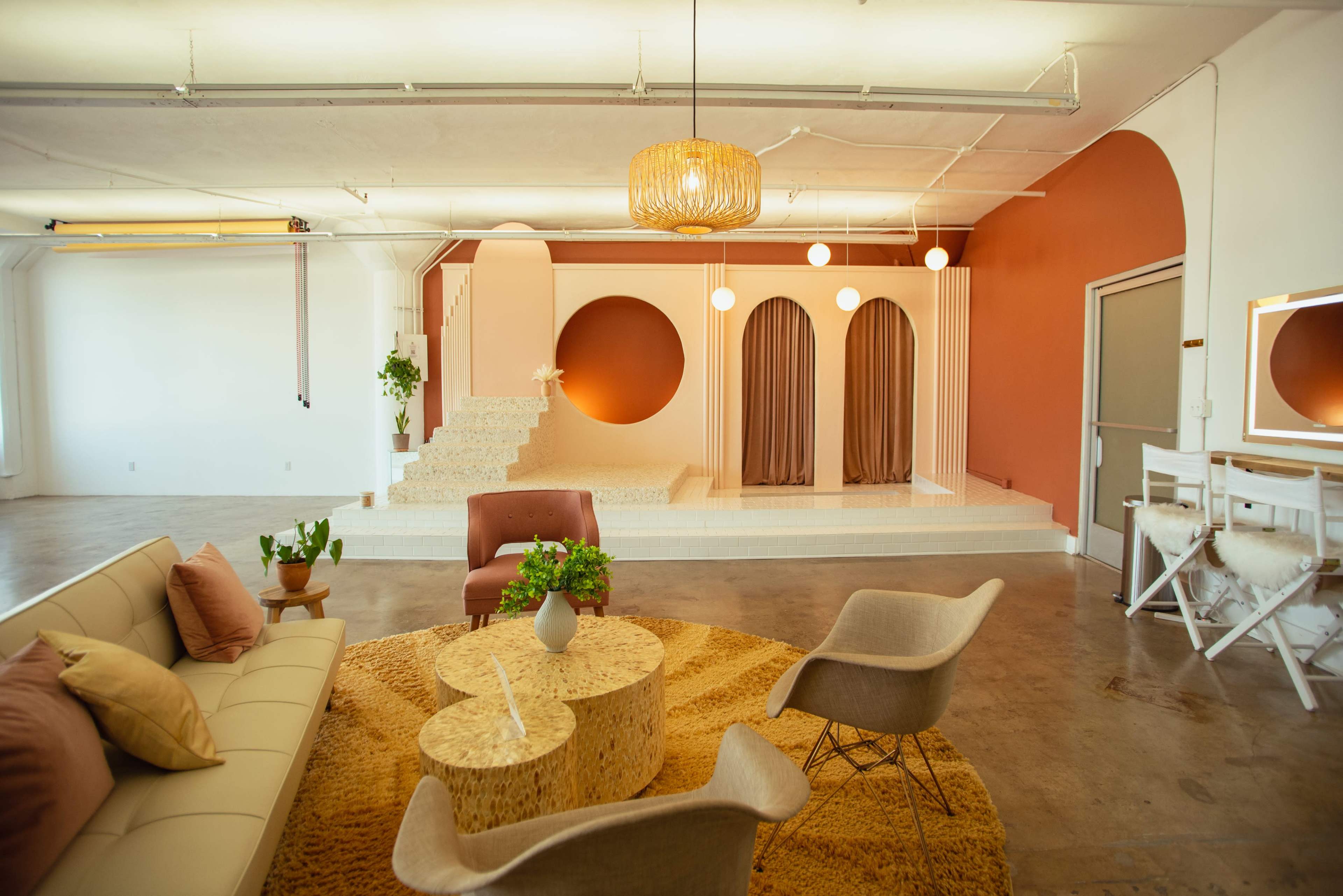A spacious interior with a seating area featuring a light-colored sofa and a round coffee table, along with a staircase leading up to a raised platform adorned with curtains and decorative elements.