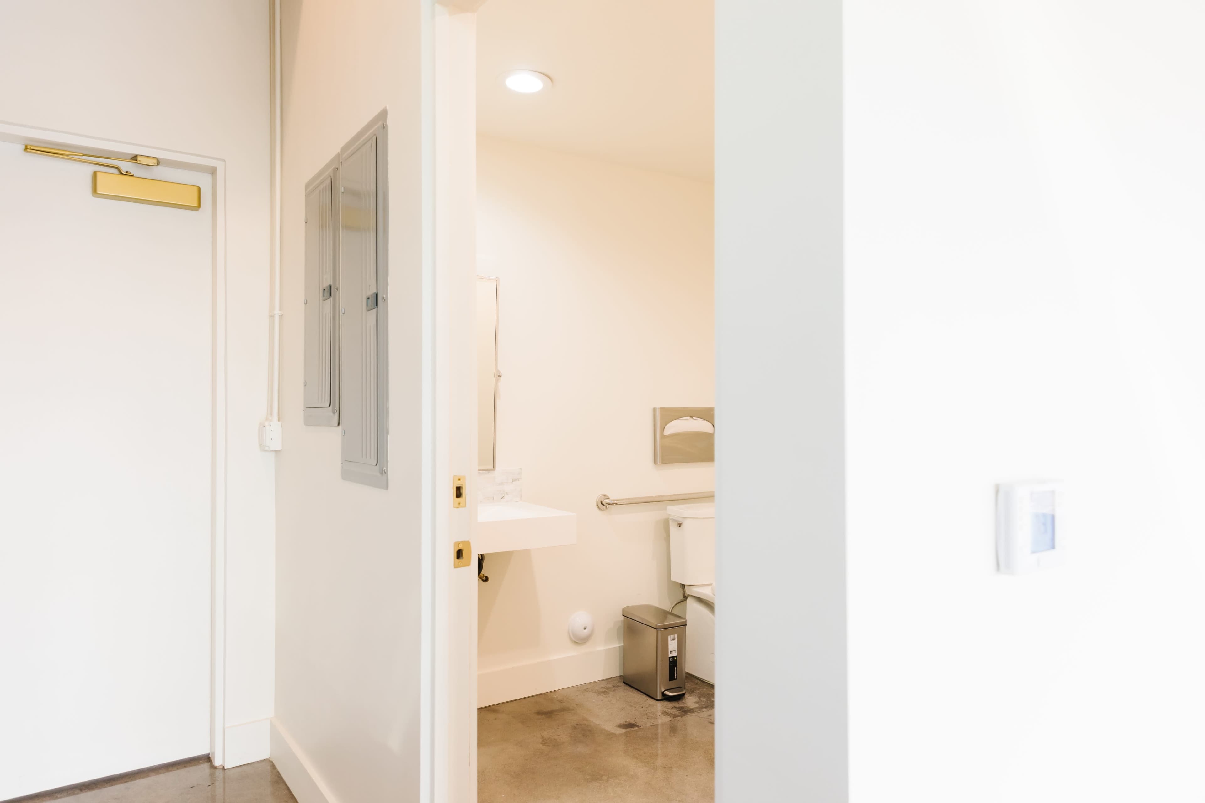 The image shows the entrance to a restroom, with a clean white interior and visible fixtures including a sink and toilet.