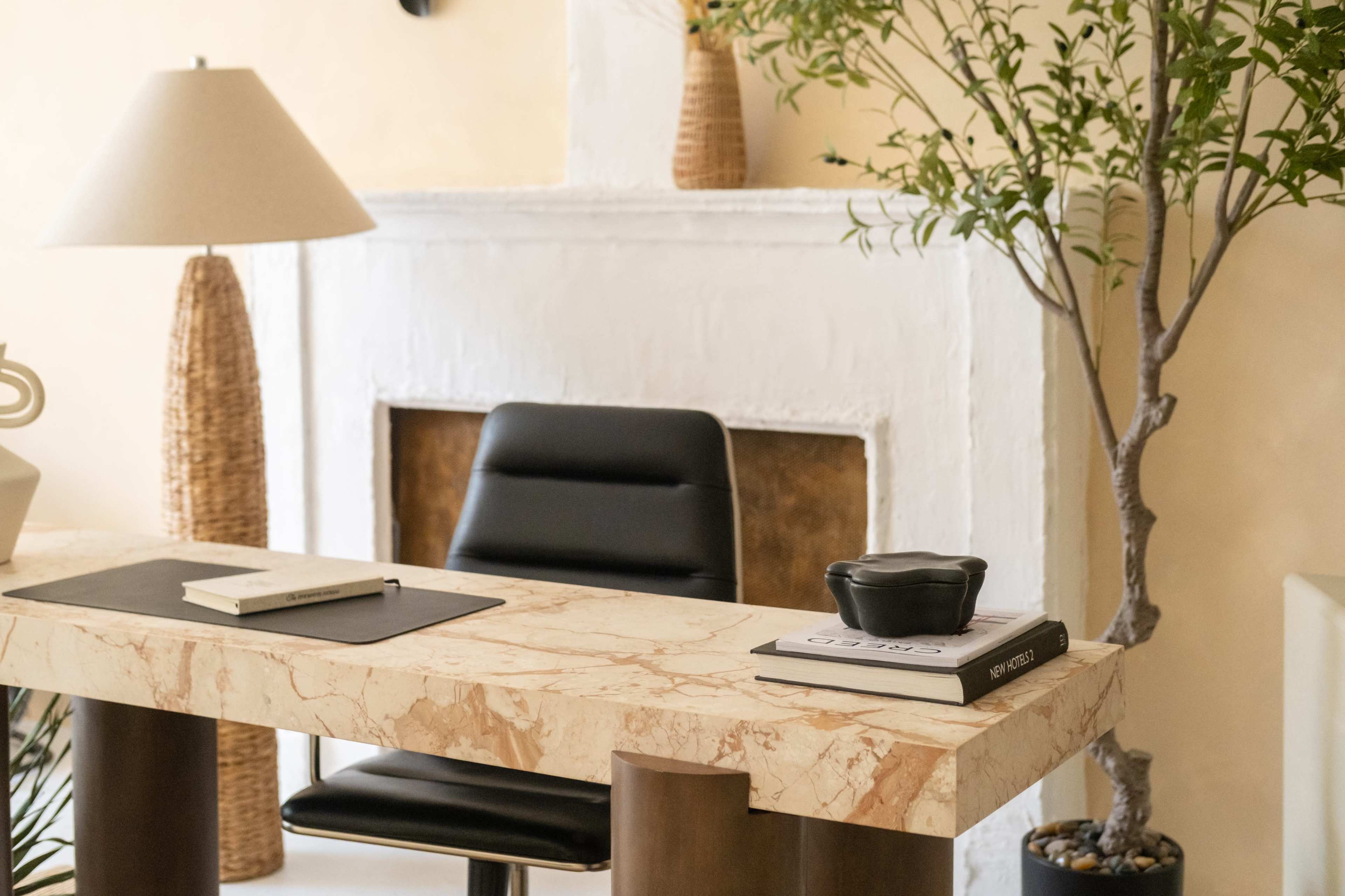 The image shows a modern workspace featuring a marble desk, a black chair, and decorative elements like a lamp and a small potted tree.