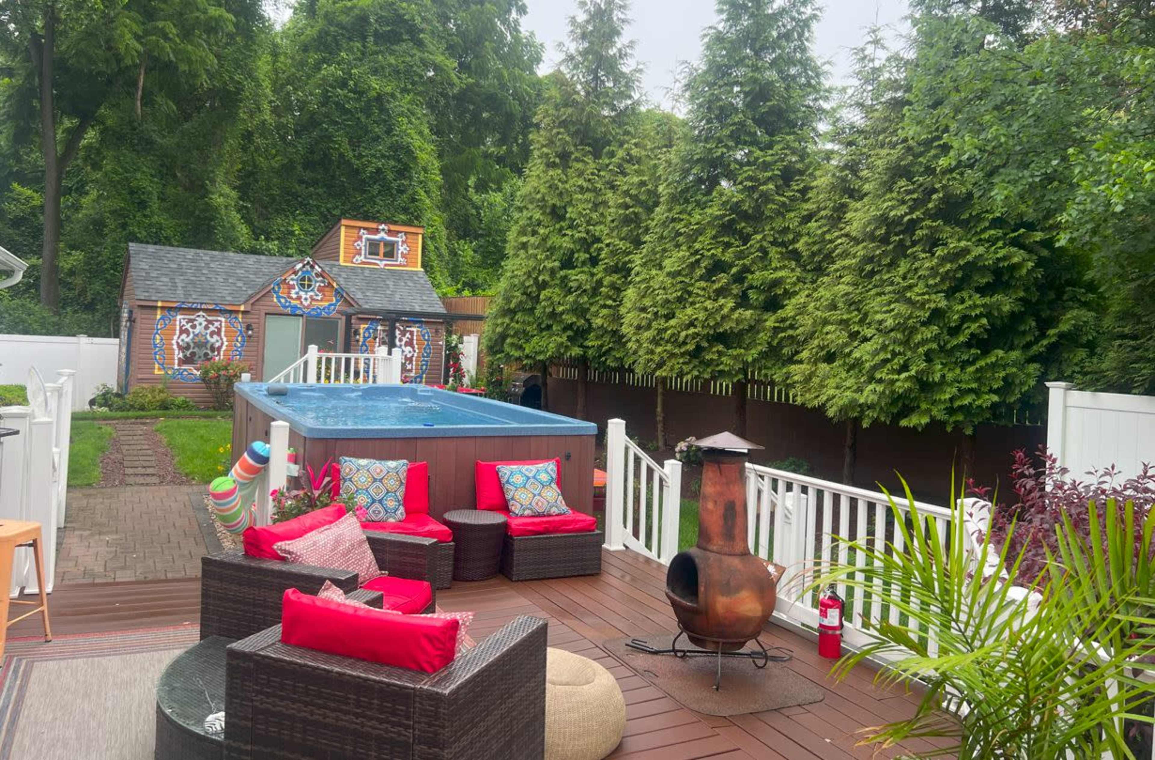 A backyard patio with a hot tub, seating area, and a colorful playhouse surrounded by lush greenery.