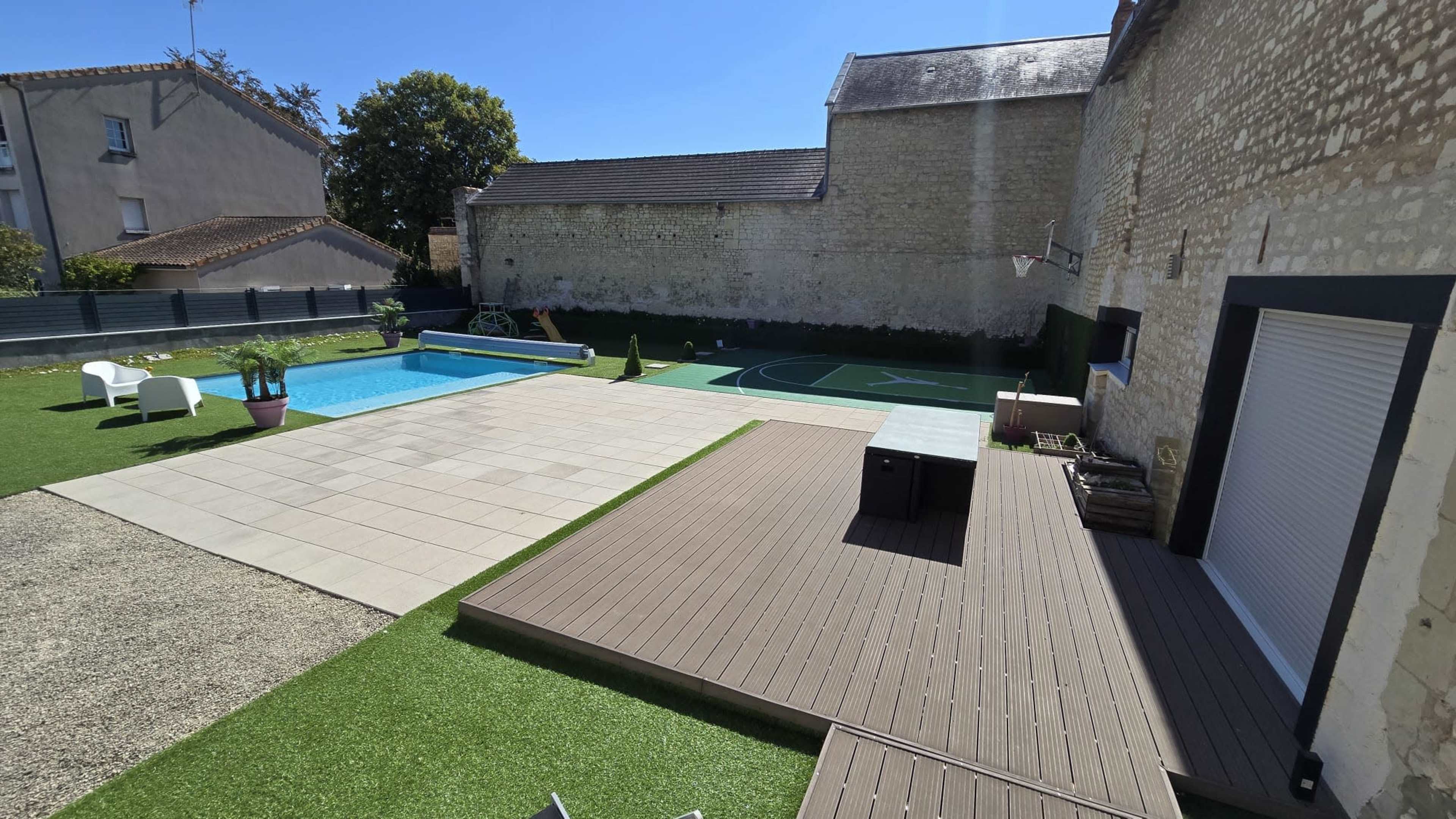The image shows a backyard with a swimming pool, a basketball court, and several lounging areas surrounded by grass and concrete paving.