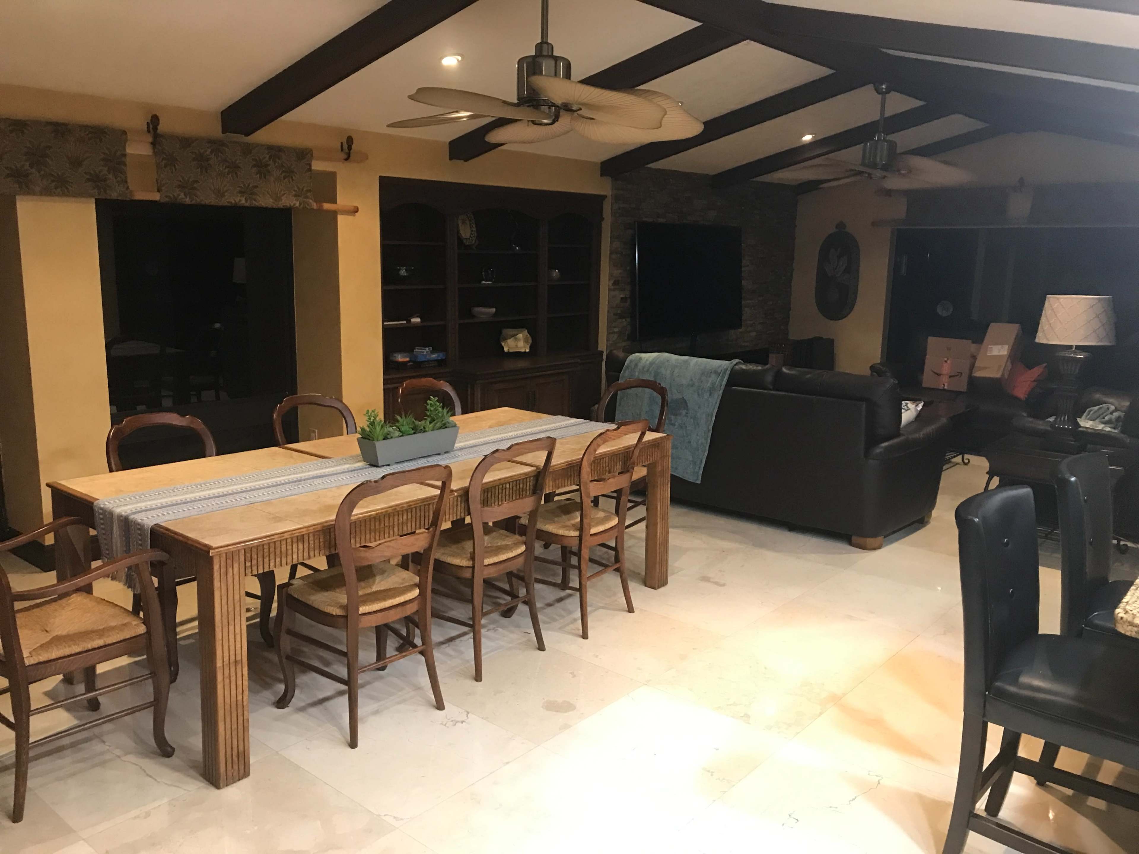 A spacious dining area with a wooden table and eight chairs is connected to a living room featuring a black sofa and a television.