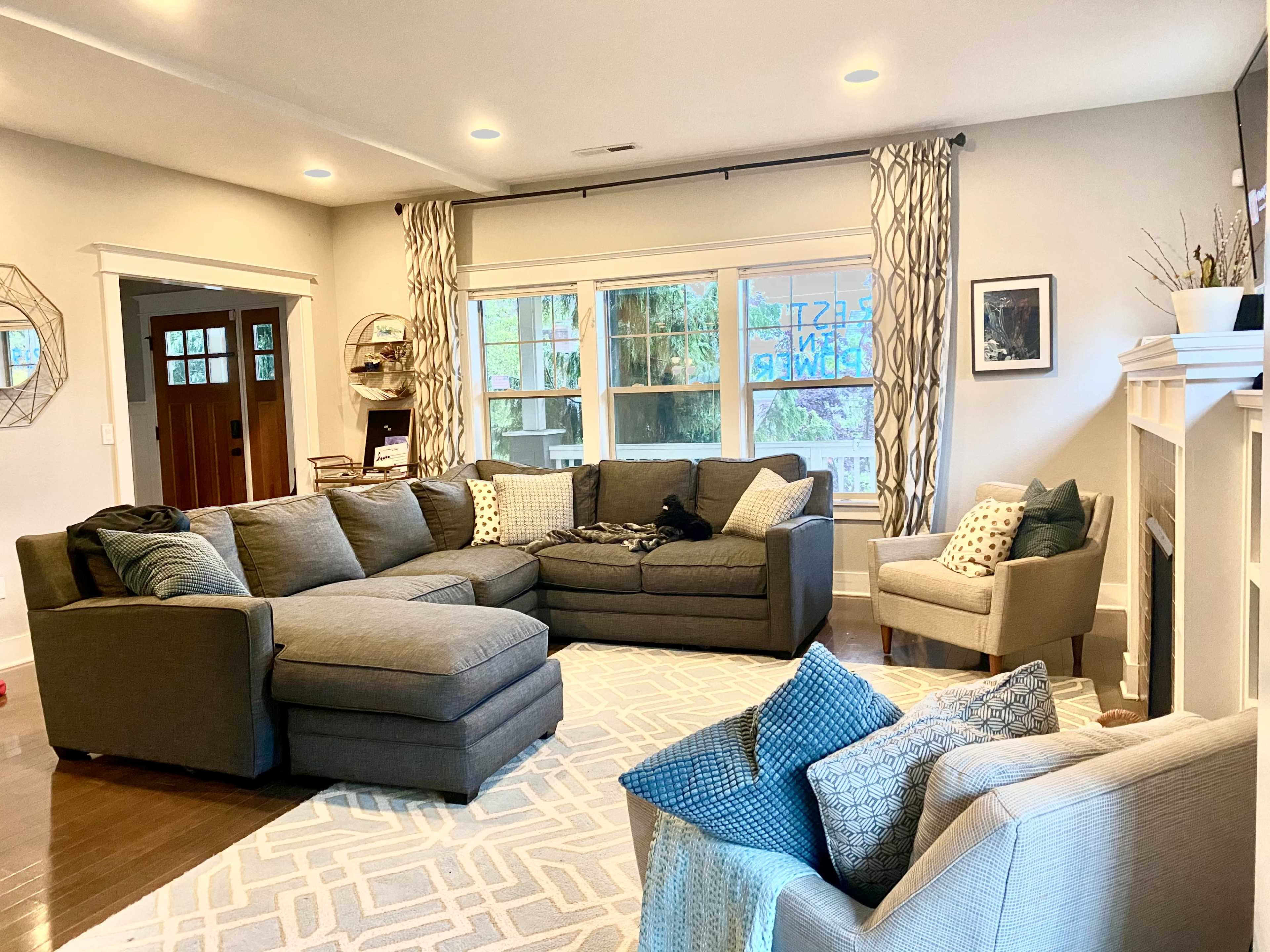 A spacious living room with a large sectional sofa, an armchair, and a decorative fireplace, all arranged around a geometric area rug.