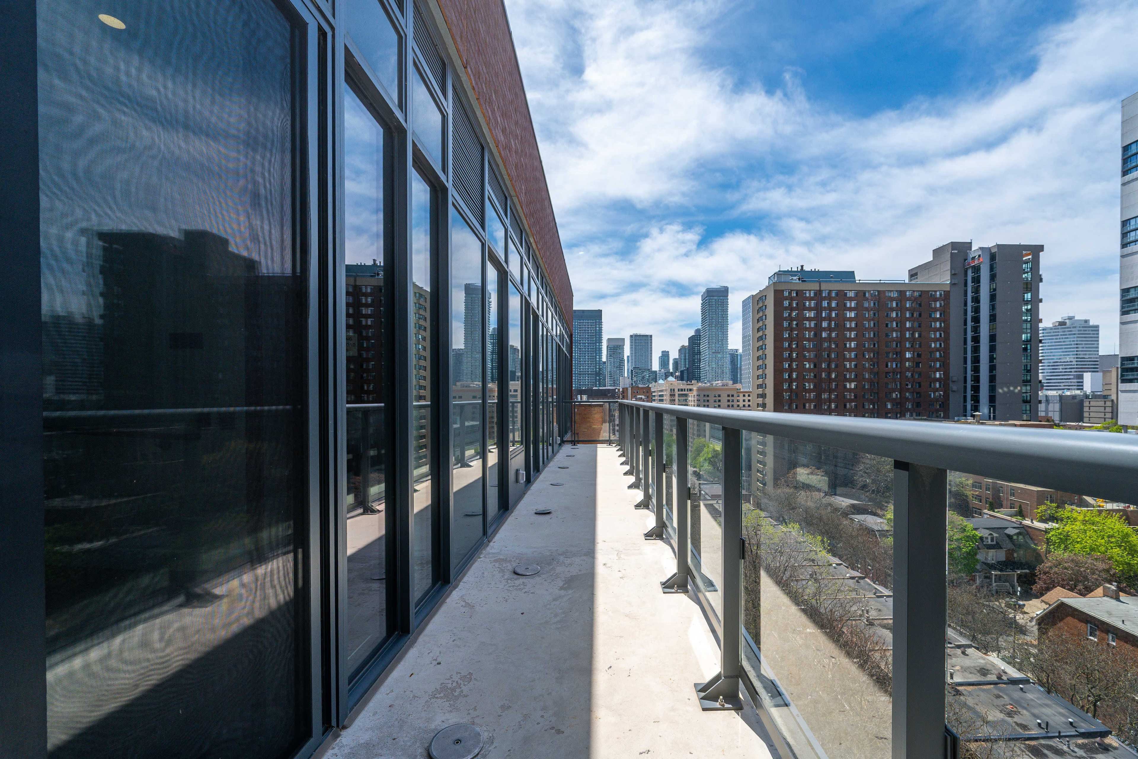 A narrow balcony overlooks a cityscape filled with tall buildings and a clear blue sky.