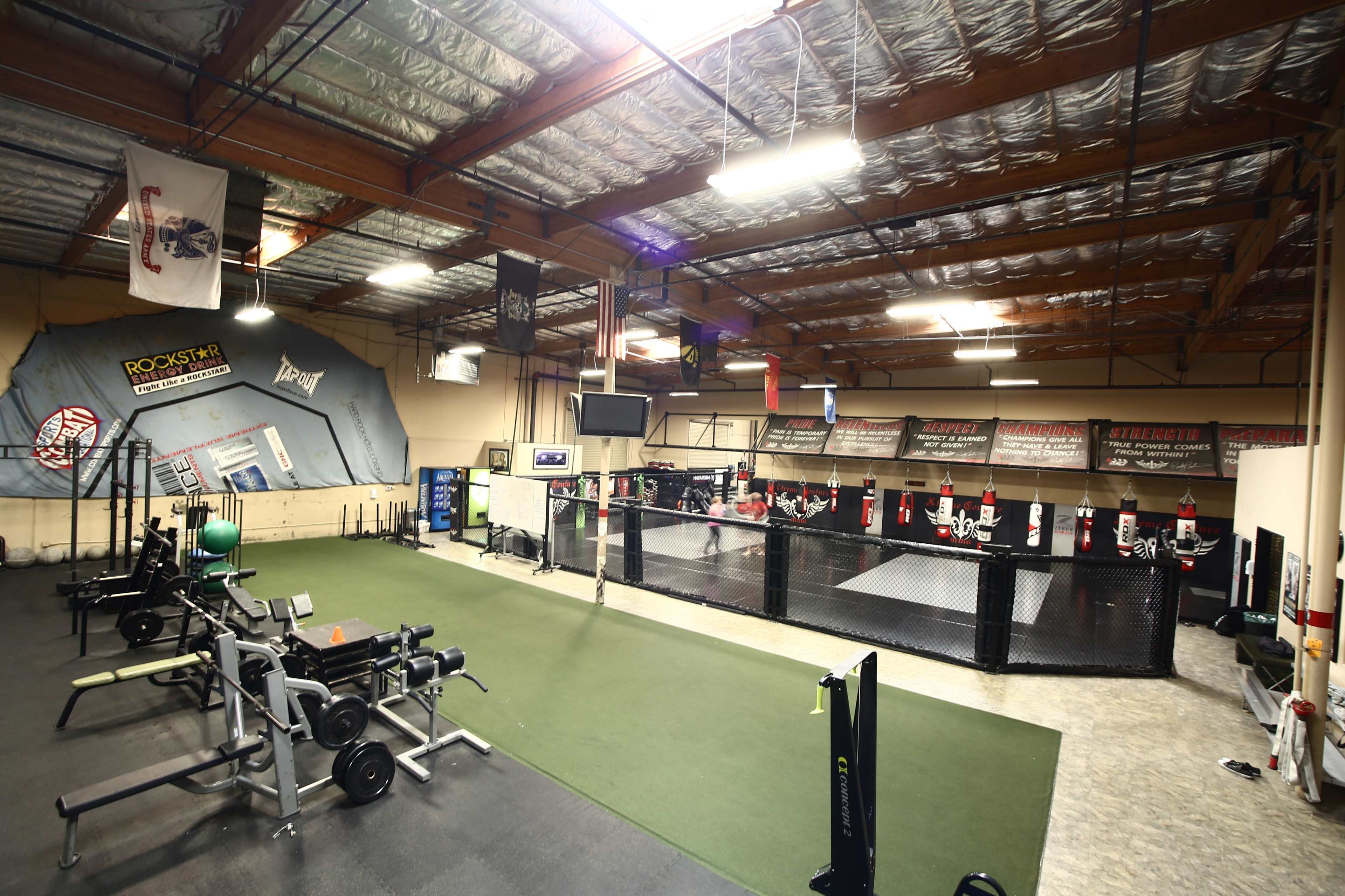 An indoor gym with exercise equipment on one side and a fenced training area on the other.