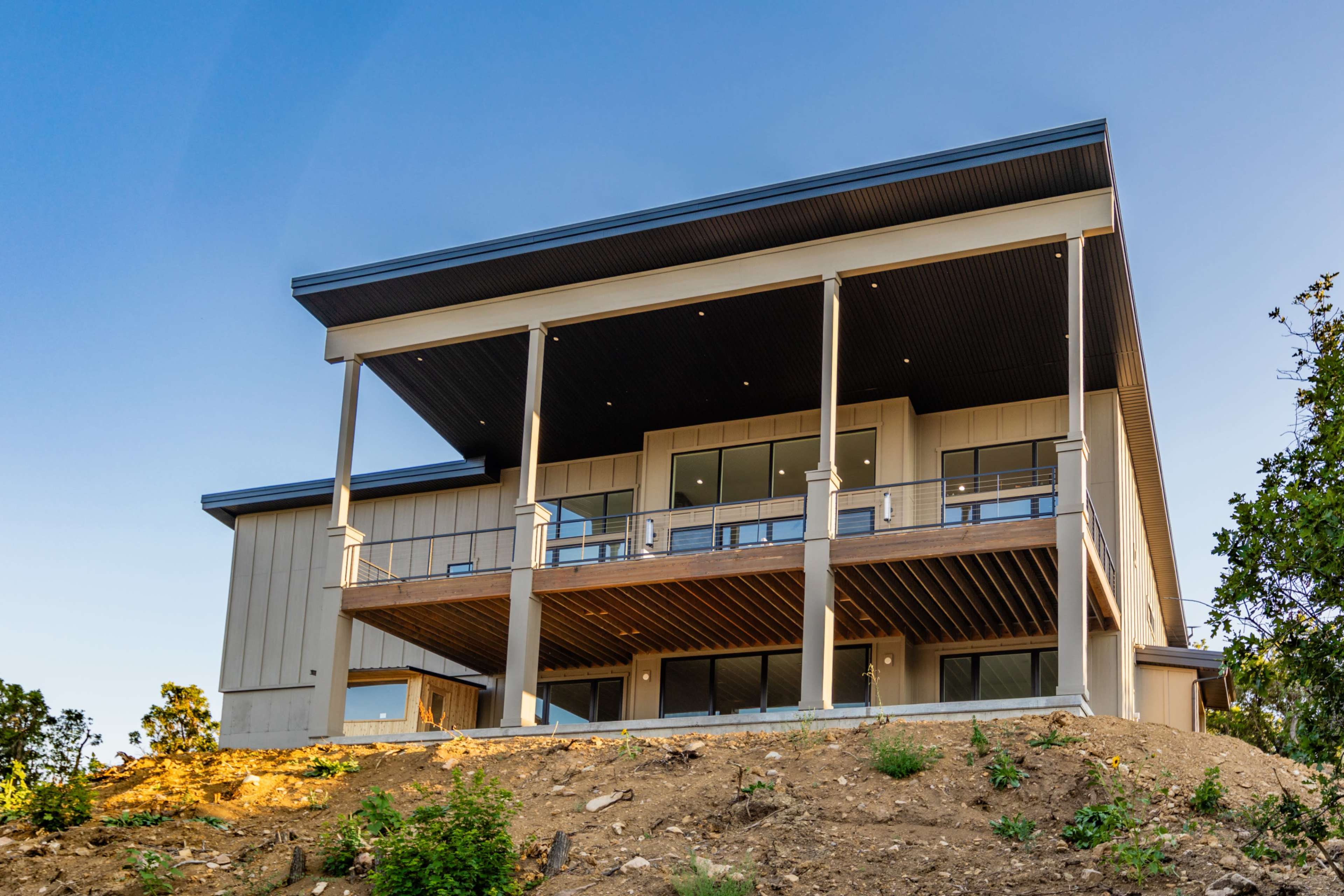 A modern house with a multi-level design features large windows and a spacious balcony, situated on a sloped area.