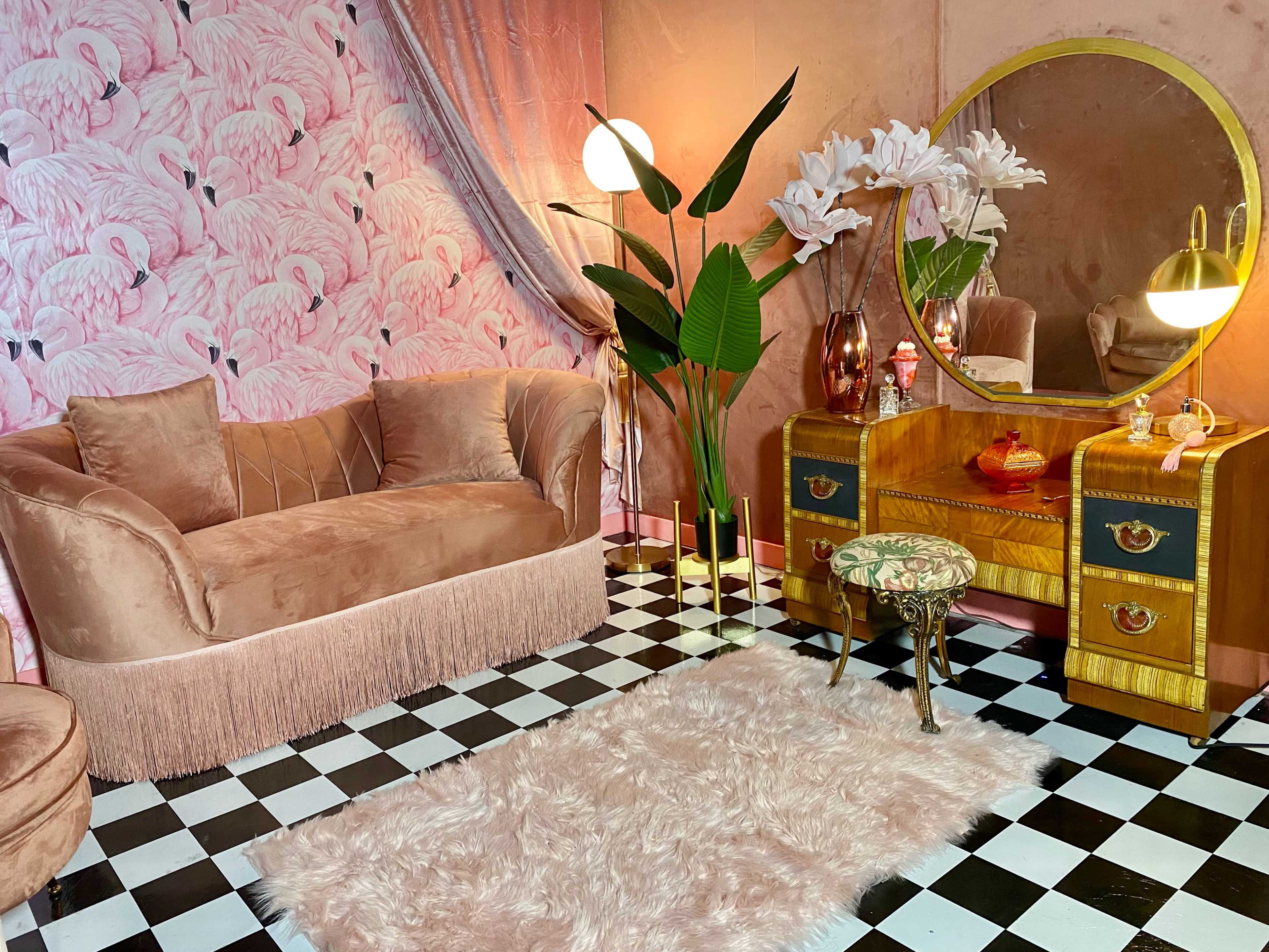 The scene features a vintage-inspired room with a pink velvet couch, a mirrored vanity, a patterned wall, and a checkered floor.