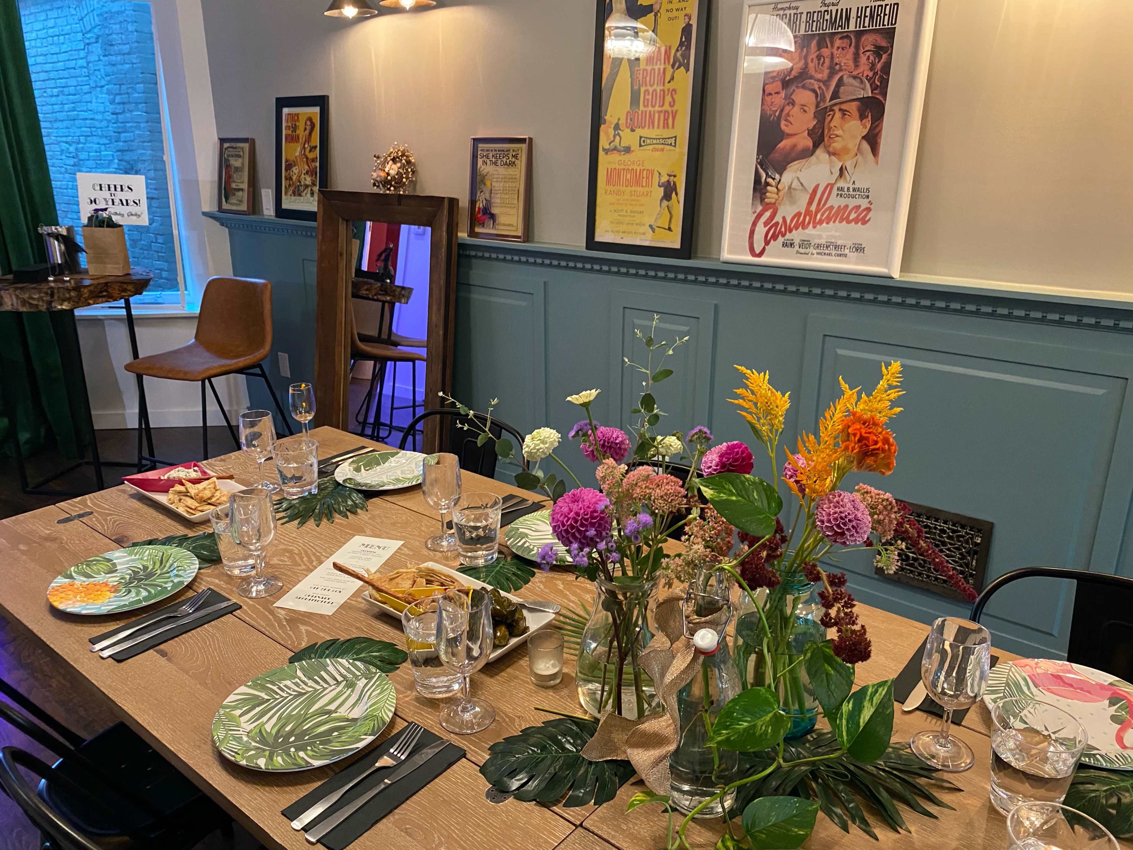 A dining table set with colorful plates, glasses, and floral arrangements, surrounded by decorative movie posters on the walls.