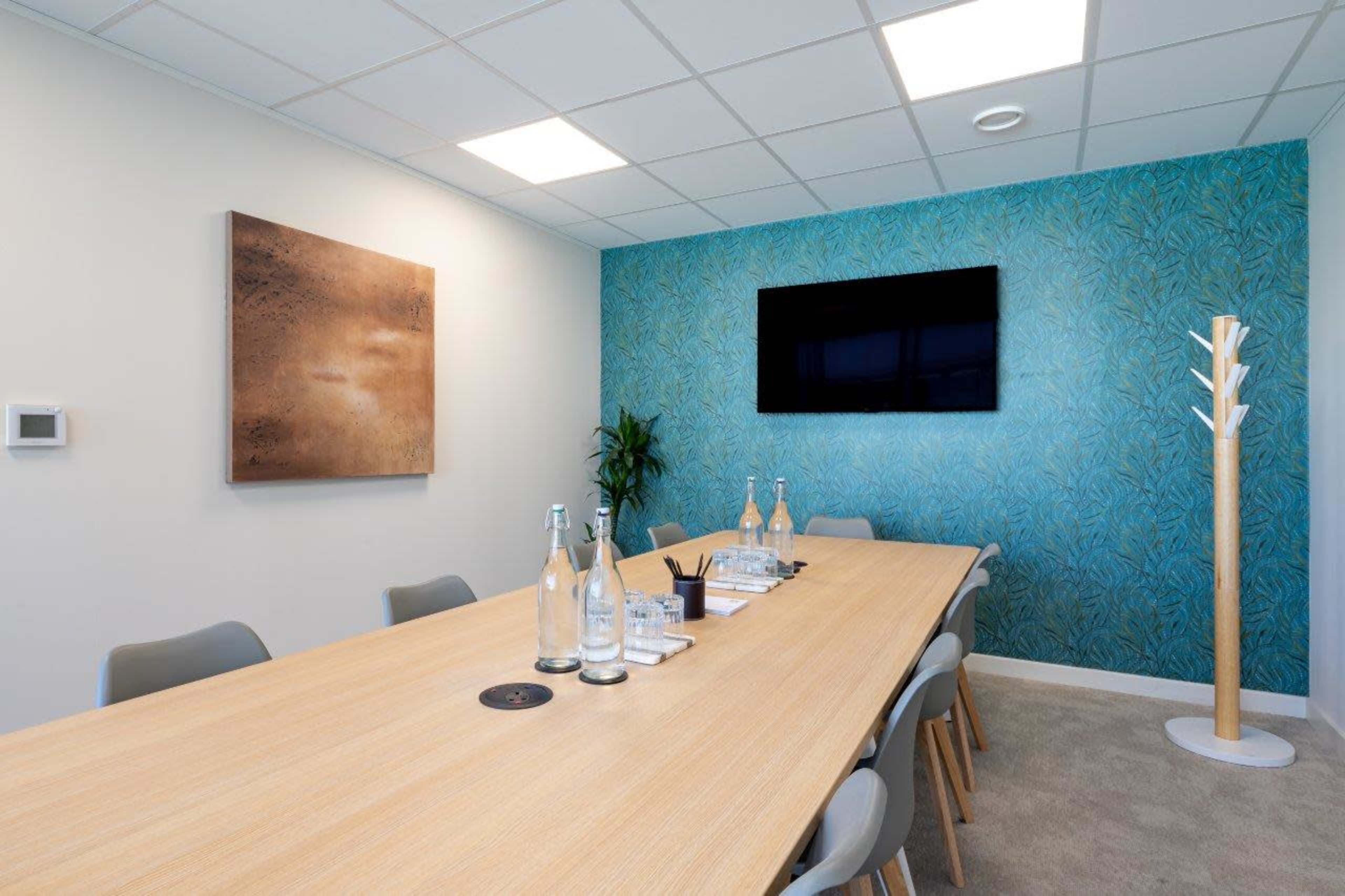 A modern conference room features a long wooden table surrounded by chairs, with a television on one wall and a decorative element on the opposite side.
