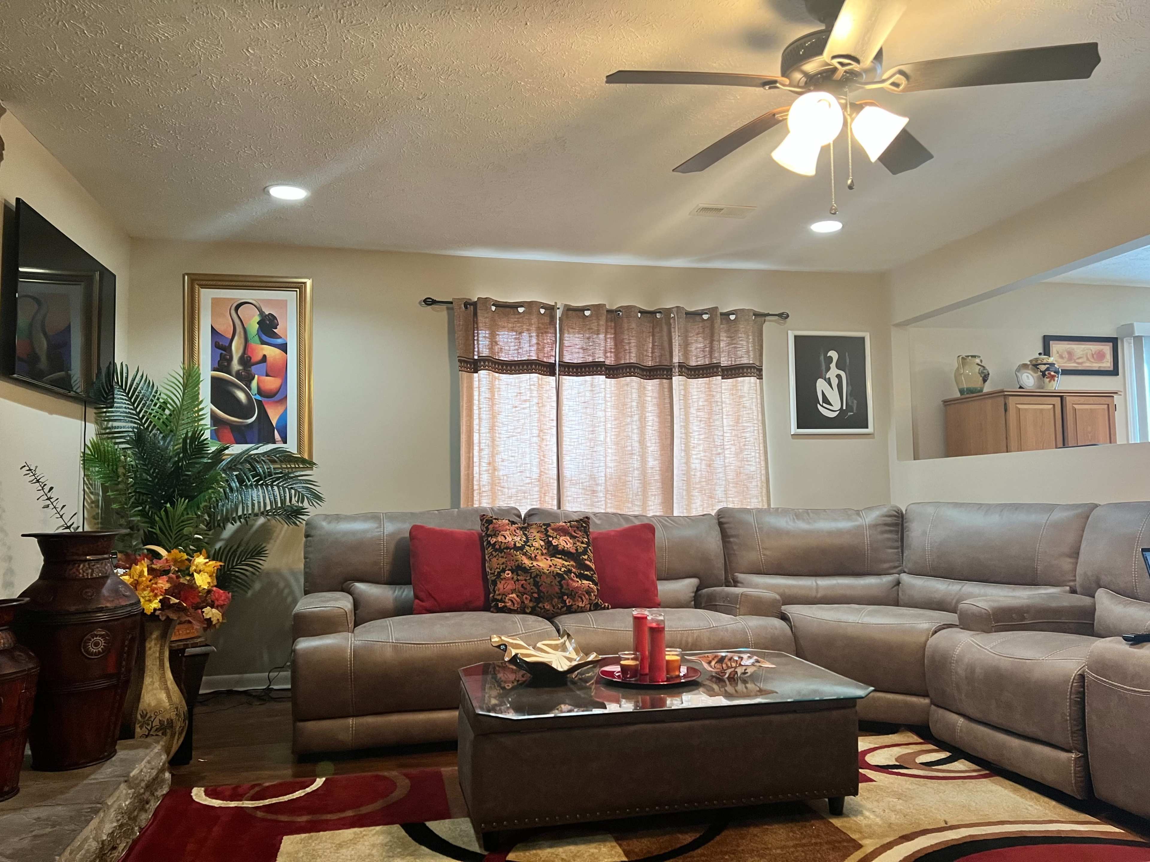 A living room with a large sectional sofa, a small coffee table, decorative art on the walls, and a window with light-colored curtains.