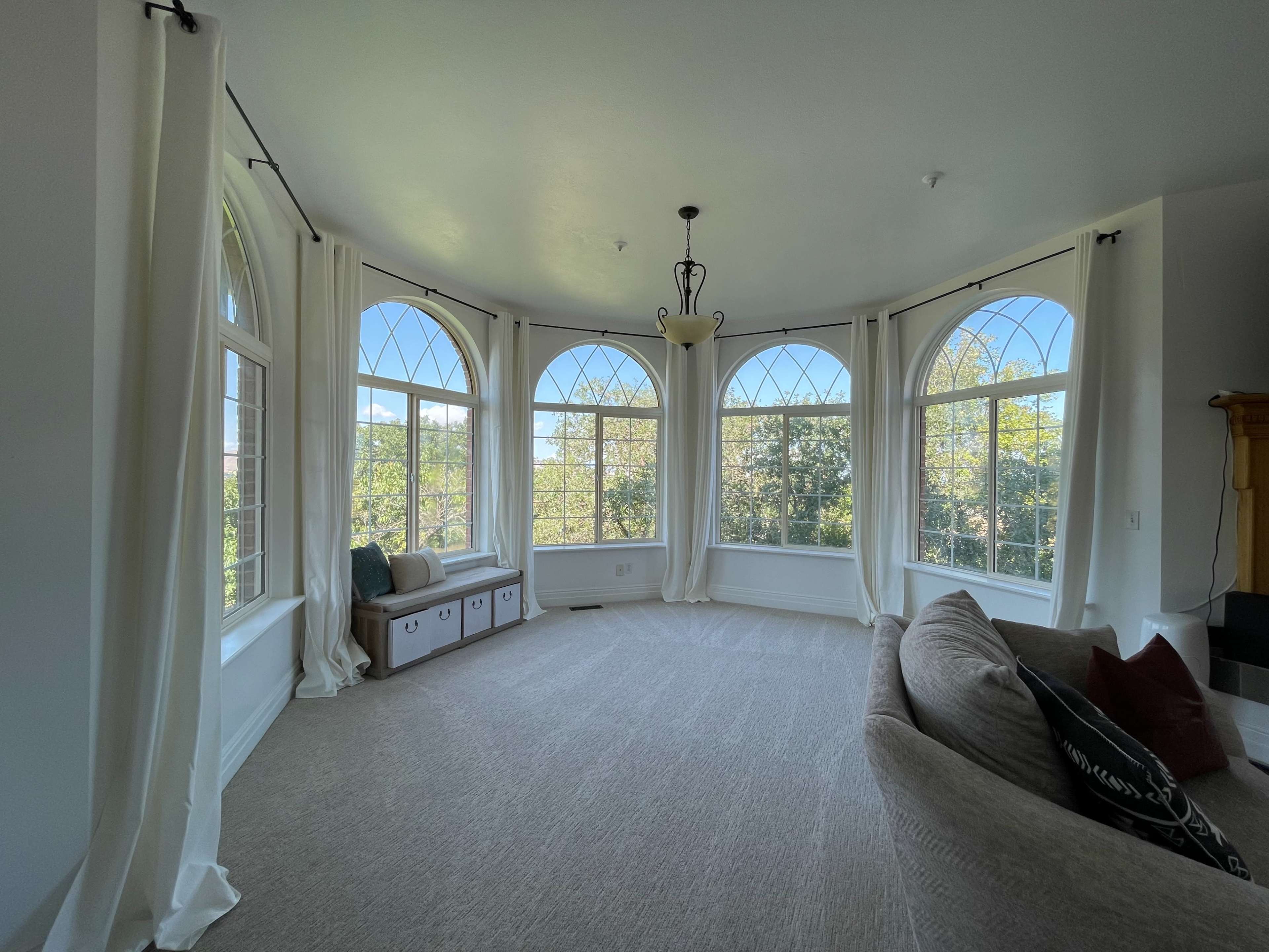 A spacious living room features large arched windows that overlook greenery, with a cozy sofa and decorative pillows arranged in the corner.