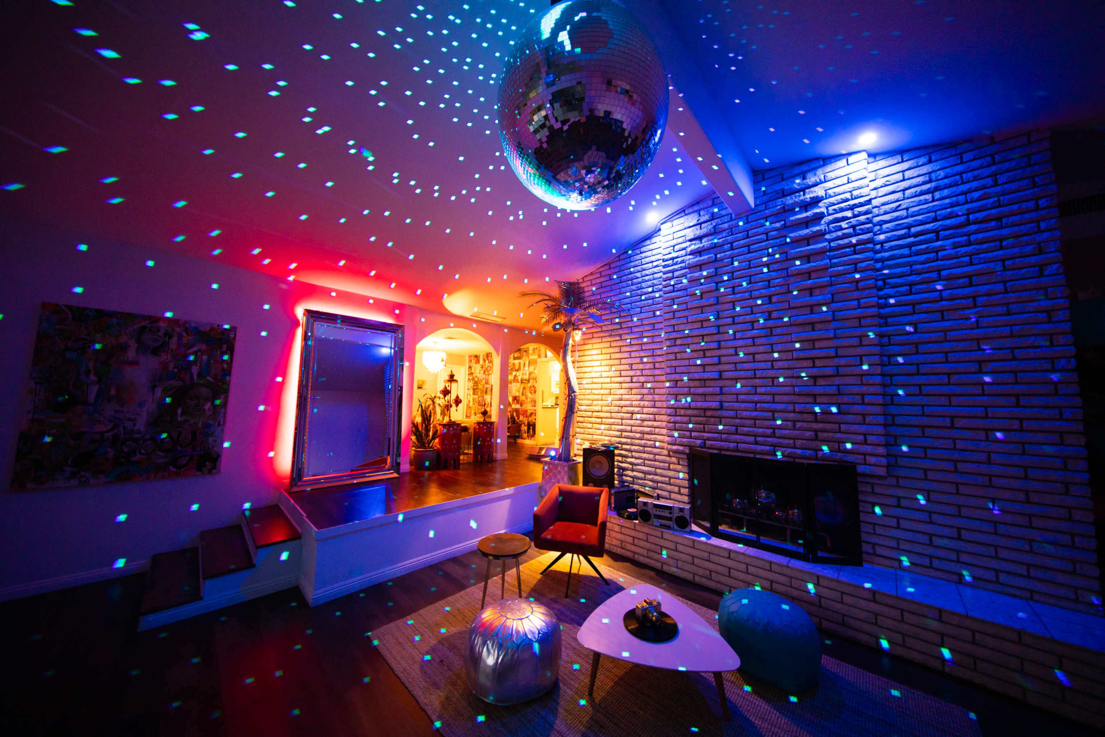 A living room features a disco ball reflecting colored lights onto the walls, with modern furniture and a fireplace.