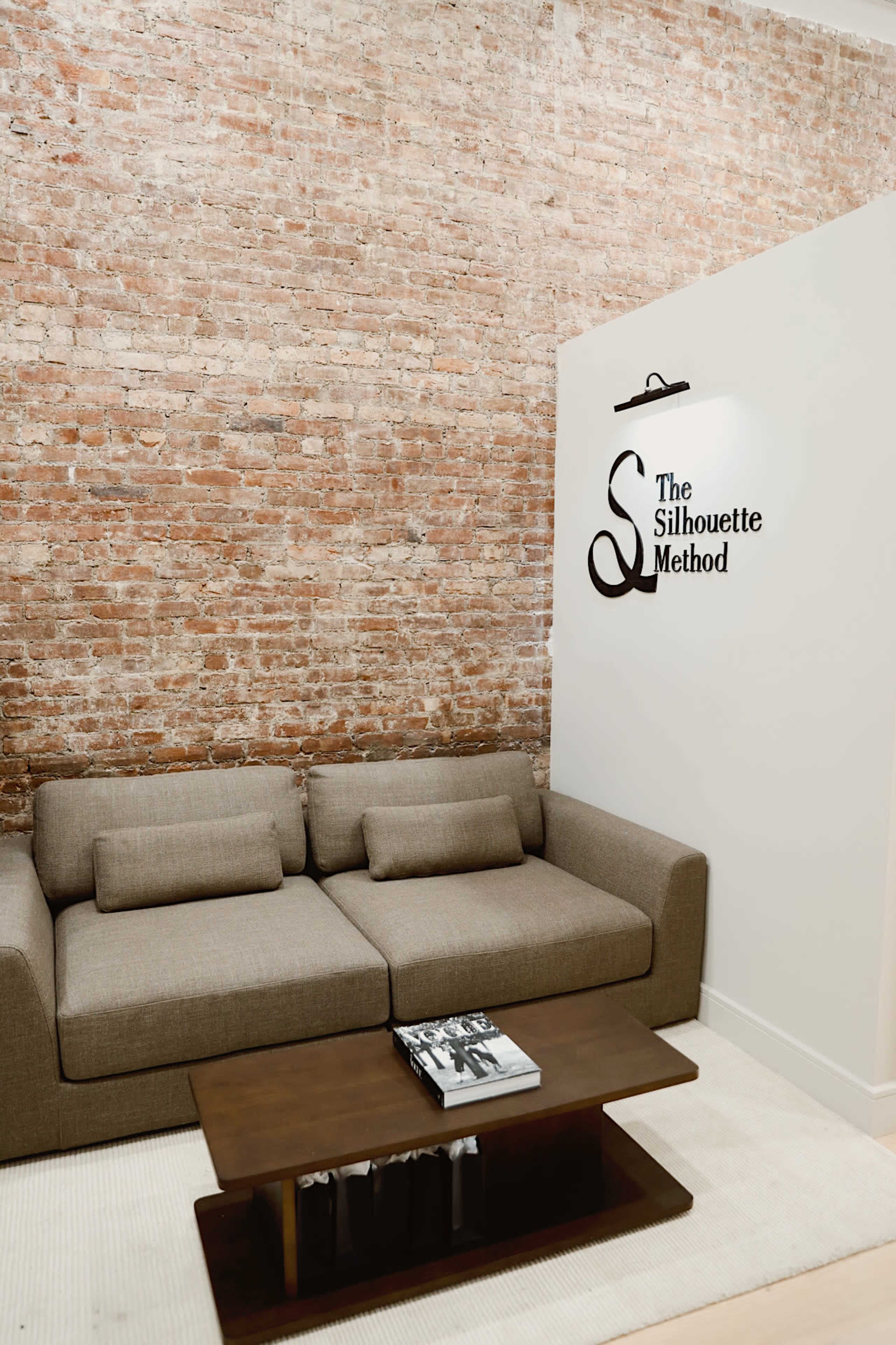 The image shows a modern interior with a brown brick wall, a gray sofa, a dark wood coffee table, and a sign that reads "The Silhouette Method."