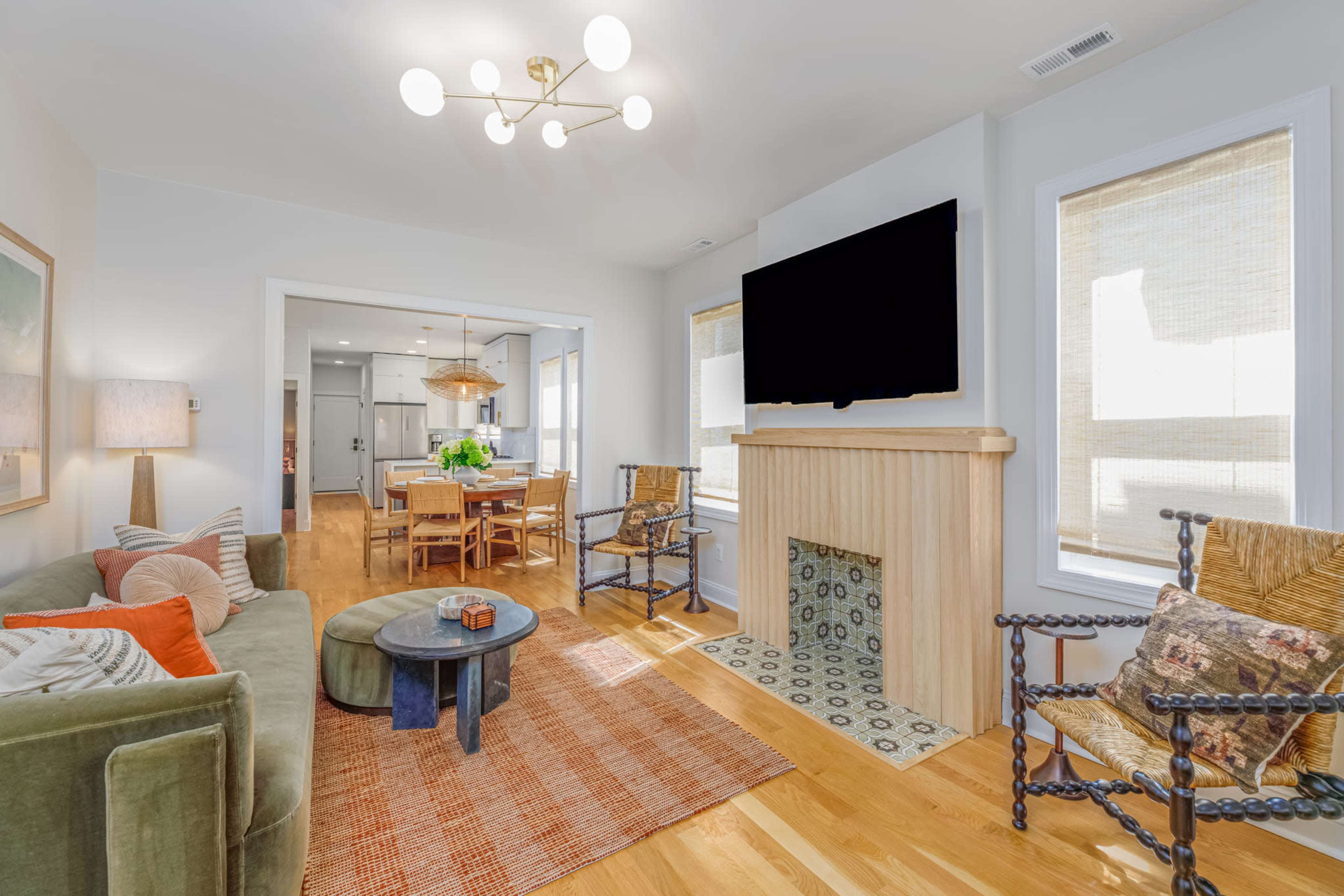 The room features a cozy seating area with a green sofa and a decorative fireplace, while a dining table is visible in the background.