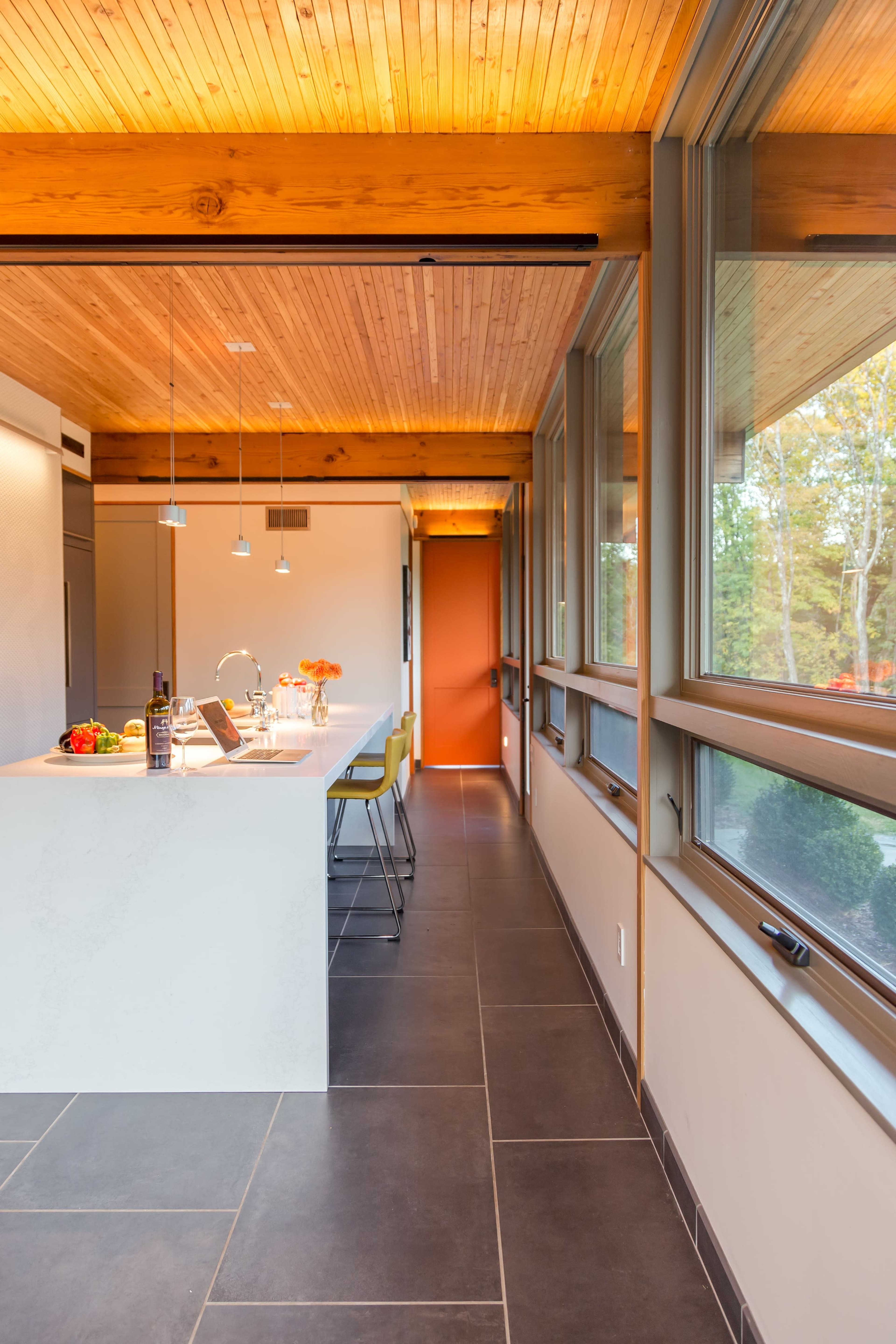 A modern kitchen features a white island with bar stools, large windows, and wooden ceiling beams.