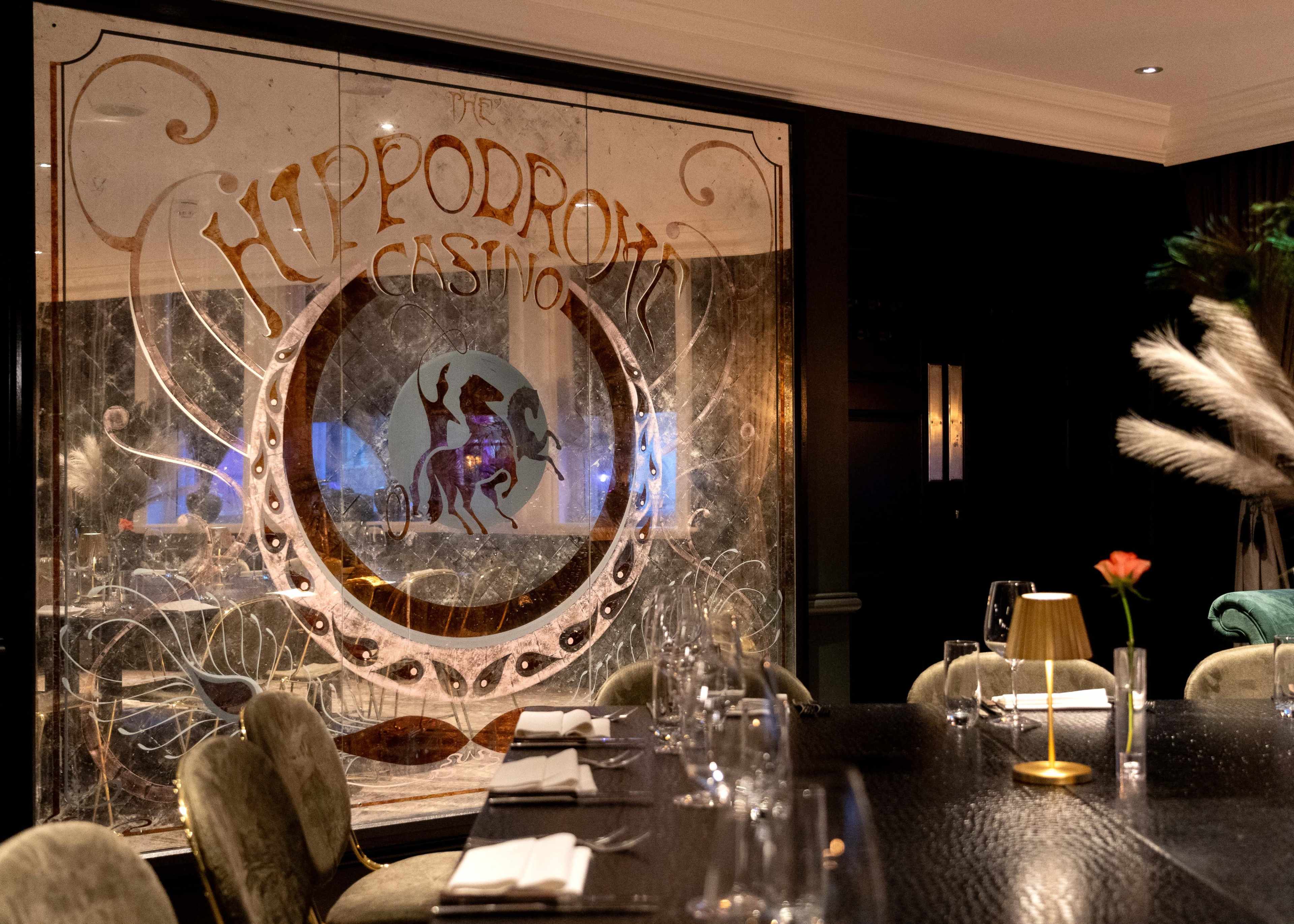 The image shows the interior of a restaurant with a decorative glass partition featuring the words "Hippodrome Casino" and a horse illustration.