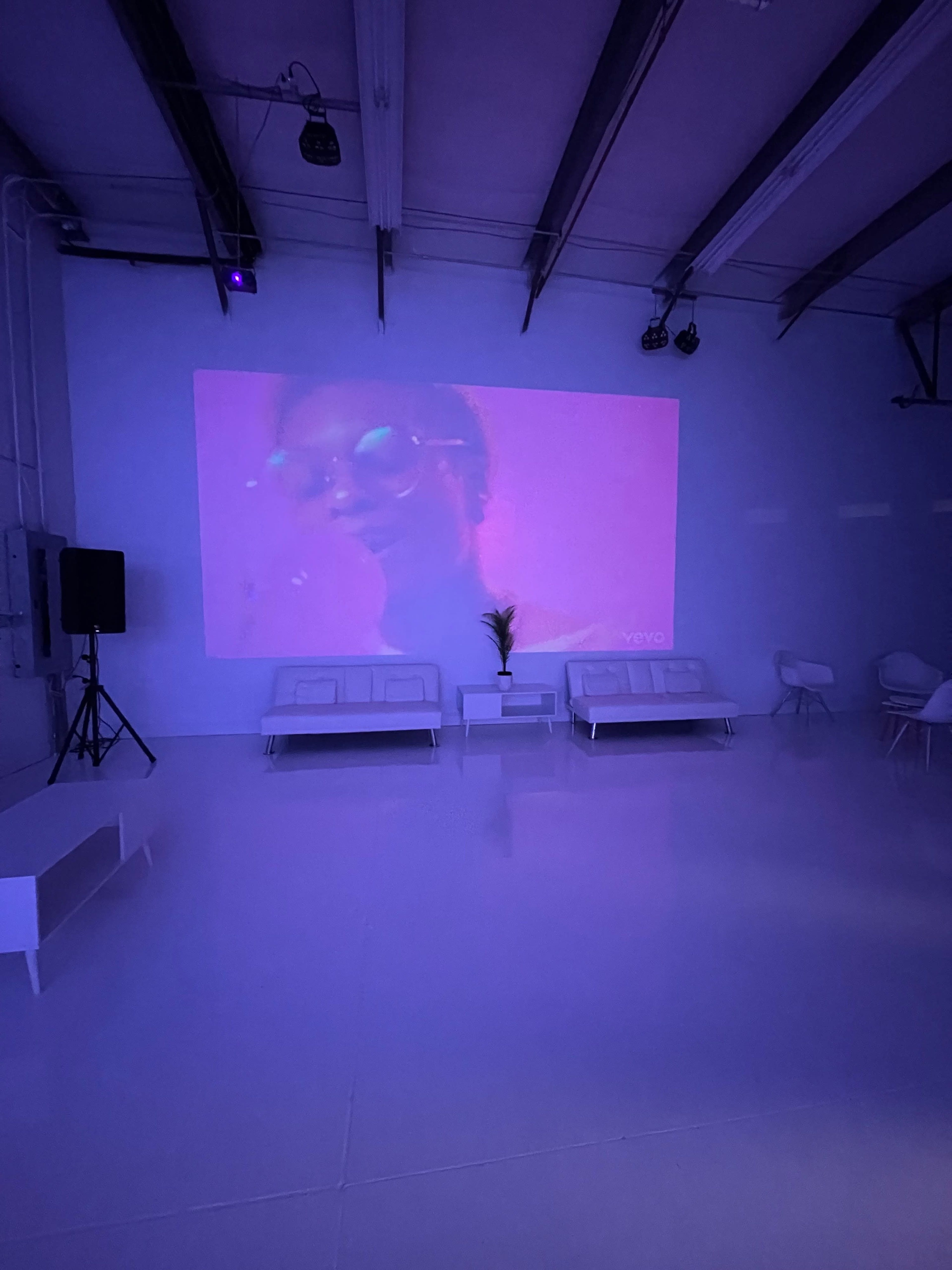 A modern, minimalist room with a large projected screen displaying a video, white sofas, and soft lighting.
